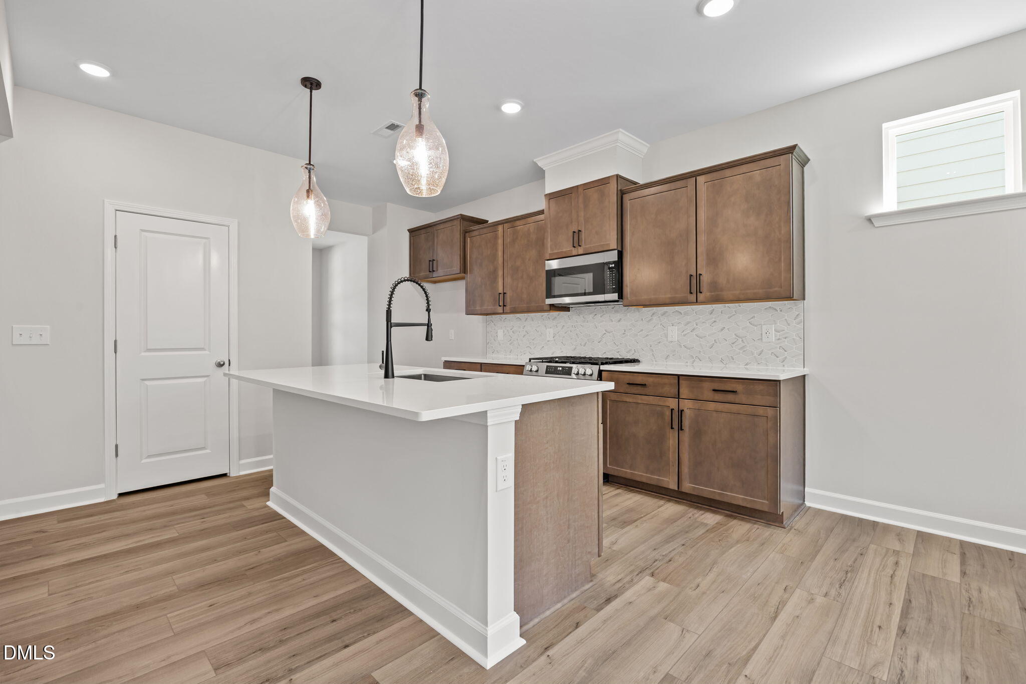 Modern kitchen featuring white quartz island, brown shaker cabinets, stainless appliances in The Willow D, Wendell, NC