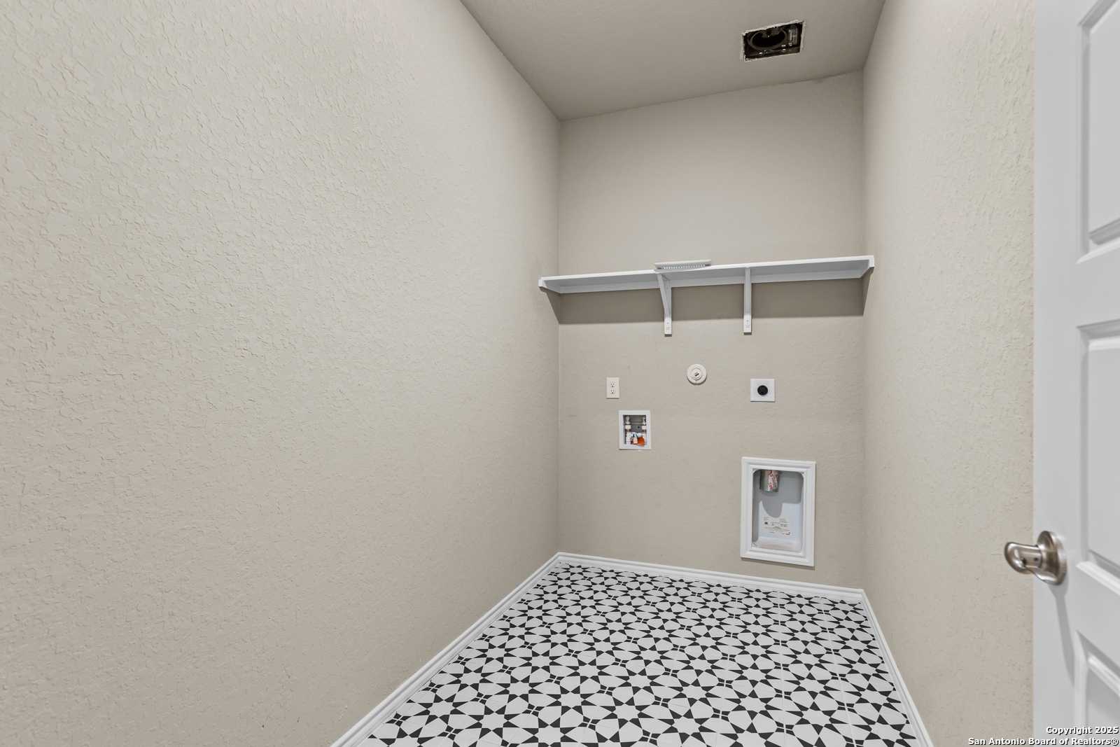 Modern laundry room with washer/dryer hookups, utility sink, open shelves, and geometric tiled floor in Davidson Homes The Douglas F, Royal Crest, San Antonio, Texas