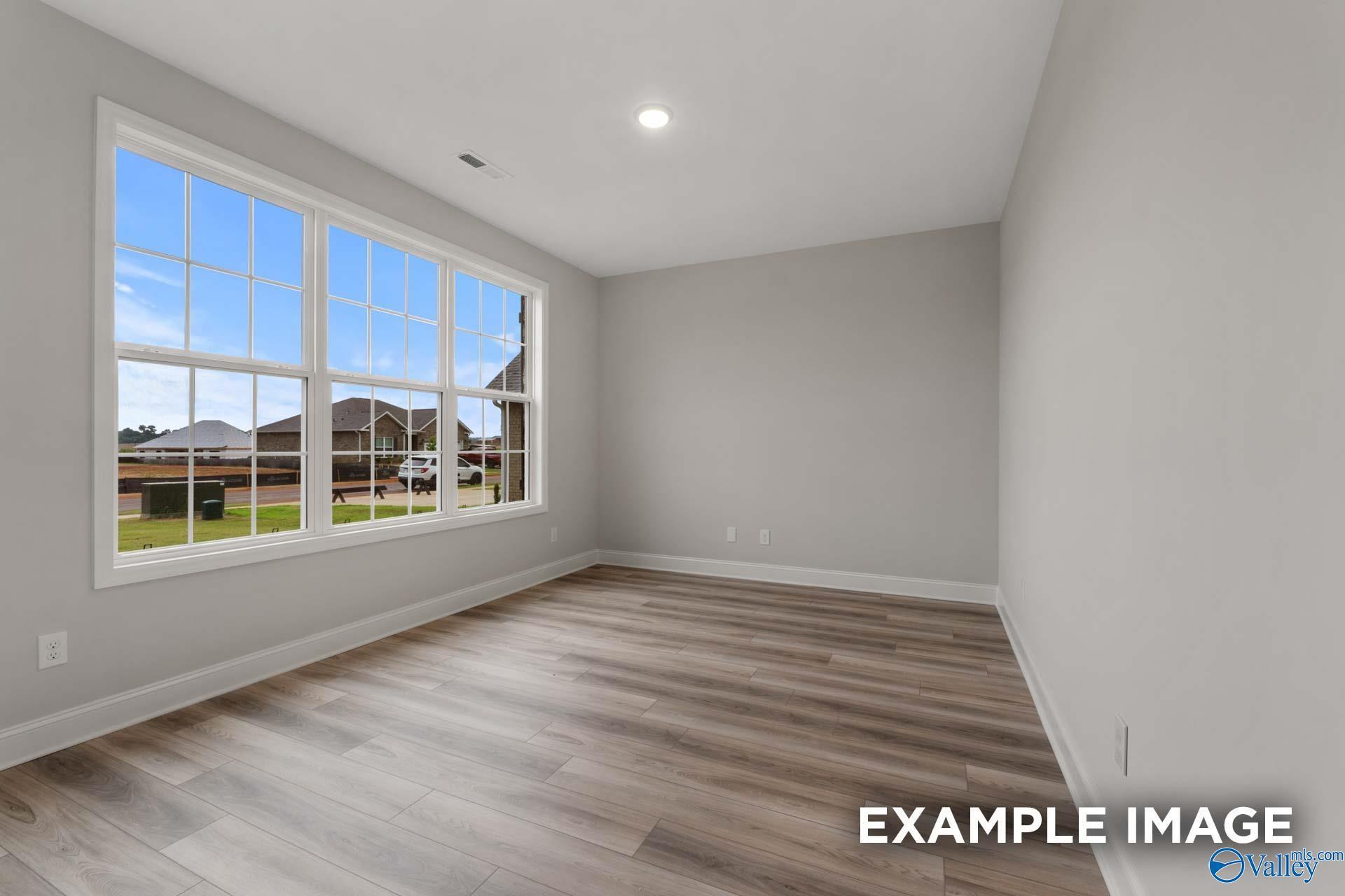 Bright bedroom with large windows, gray walls, and hardwood floors overlooking backyard in Davidson Homes The Finleigh, Meridianville, Alabama