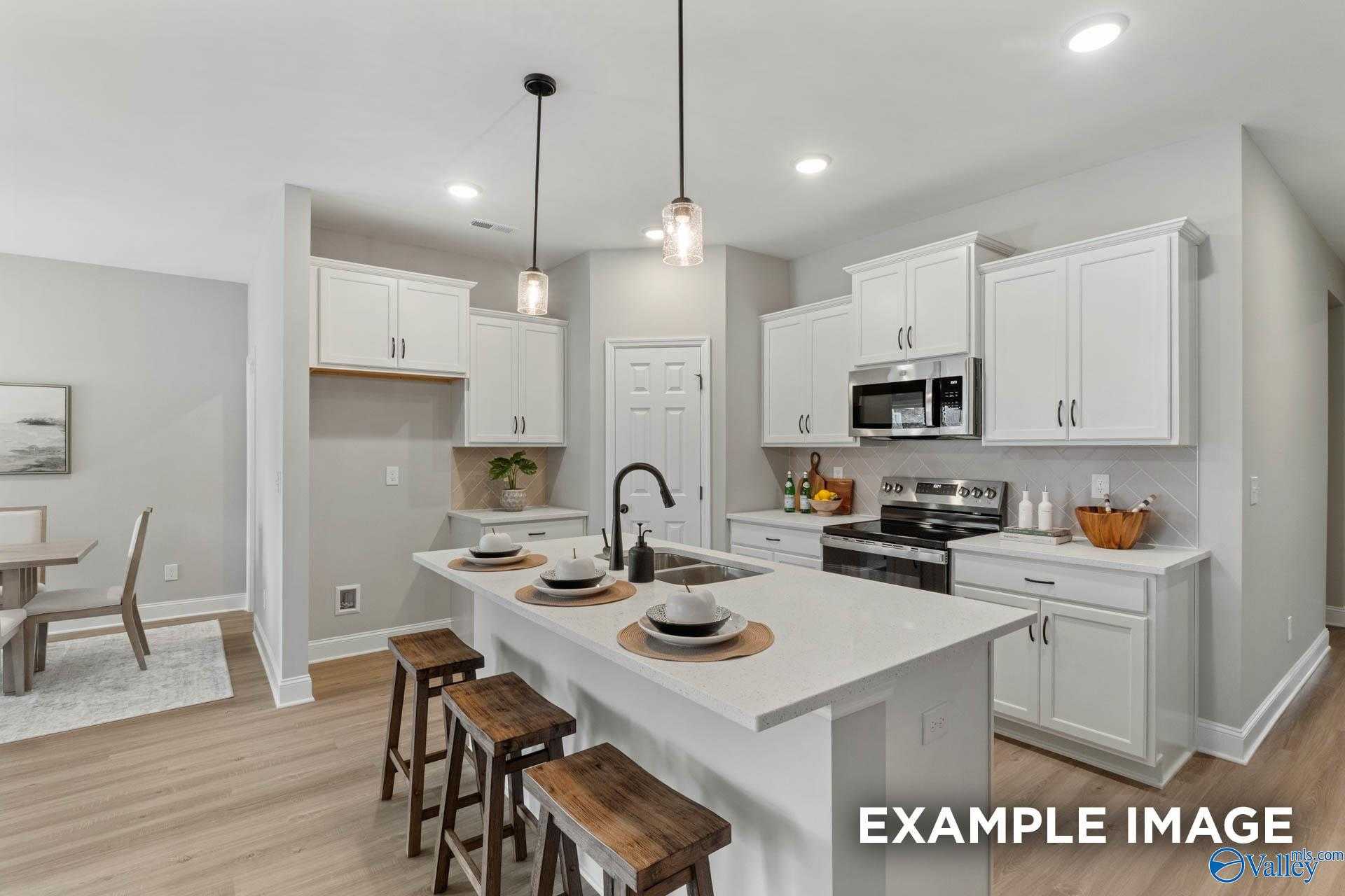 Modern white kitchen with island, stainless appliances, wooden bar stools in Davidson Homes The Daphne C, Owens Cross Roads, AL