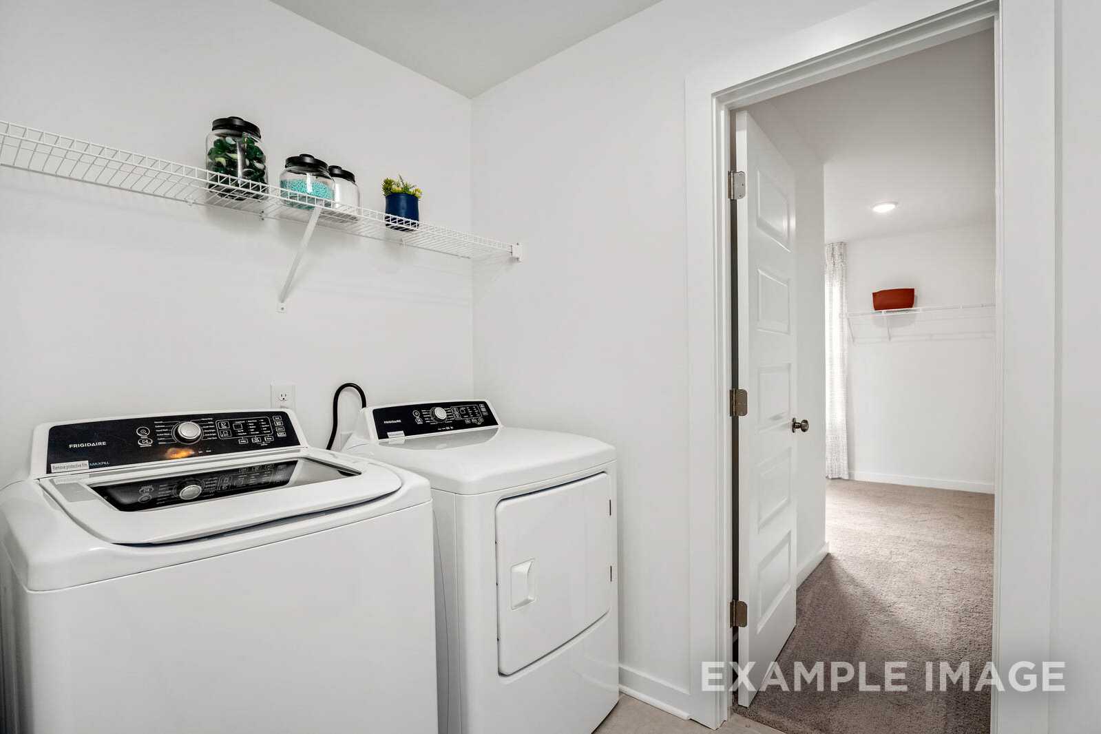 Spacious laundry room in The Gordon B by Davidson Homes with white front-load washer dryer, storage shelves, and open hallway door