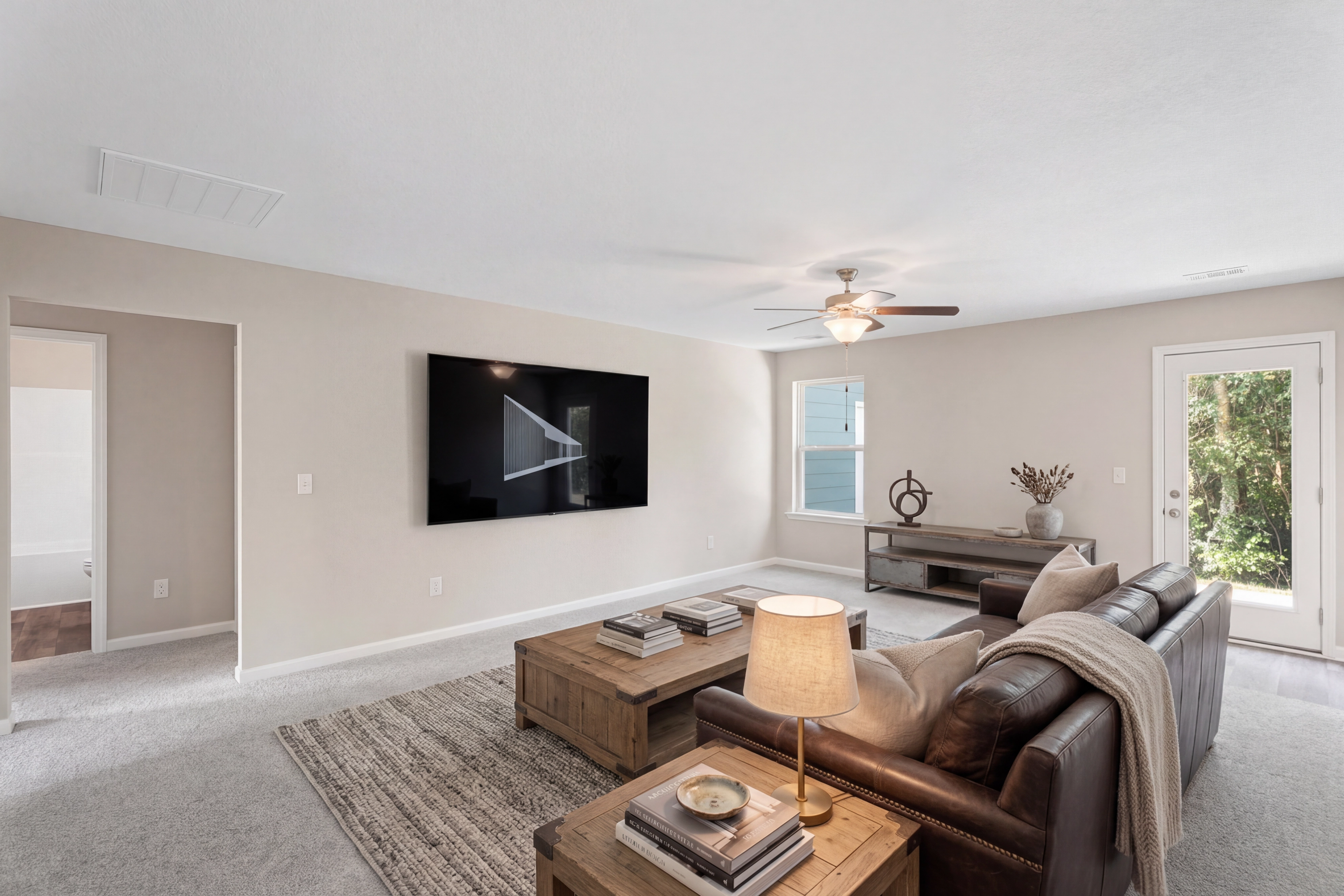 Spacious living room in Summer Vineyard, Phenix City AL by Davidson Homes with leather sofa, mounted TV, ceiling fan, and French doors