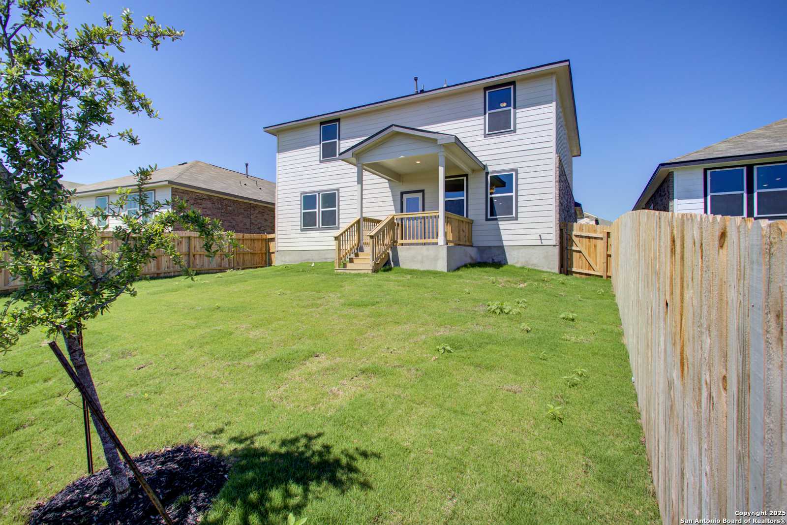 Two-story Douglas G home backyard with covered porch, deck stairs, fenced grassy yard, and trees in Comanche Ridge, San Antonio