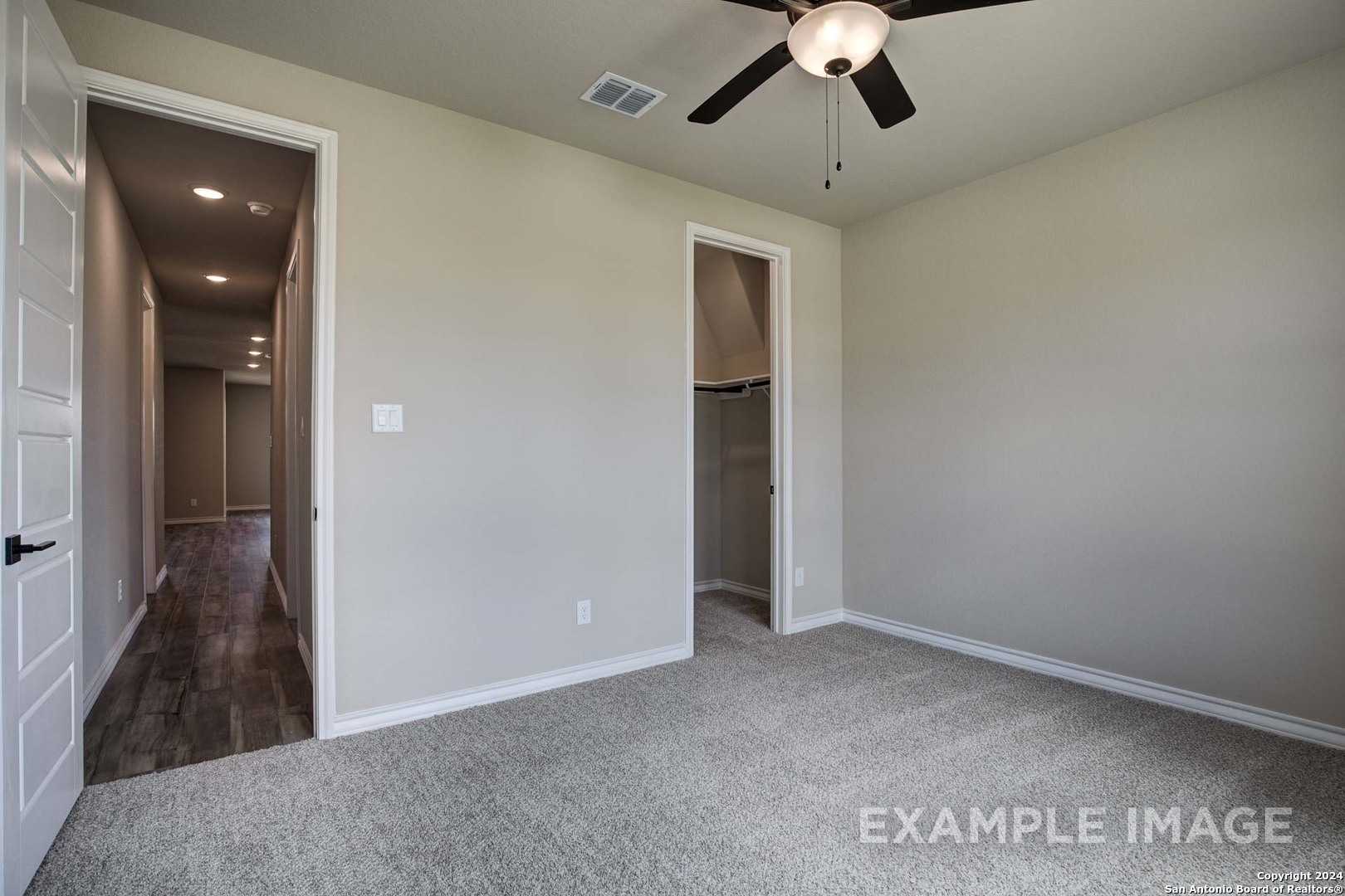 Cozy secondary bedroom with beige walls, gray carpet, ceiling fan, and adjacent closet in Davidson Homes The Rockford G, Ladera, San Antonio