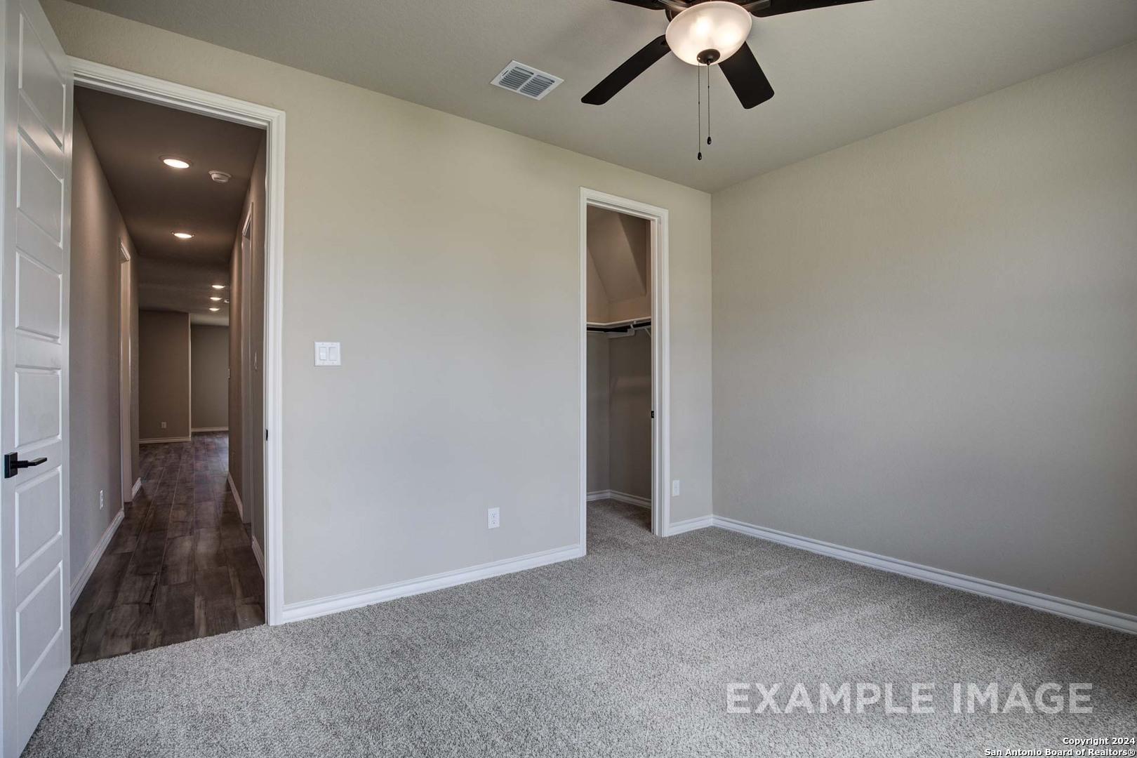 Cozy secondary bedroom with beige walls, gray carpet, ceiling fan, and adjacent closet in Davidson Homes The Rockford G, Ladera, San Antonio