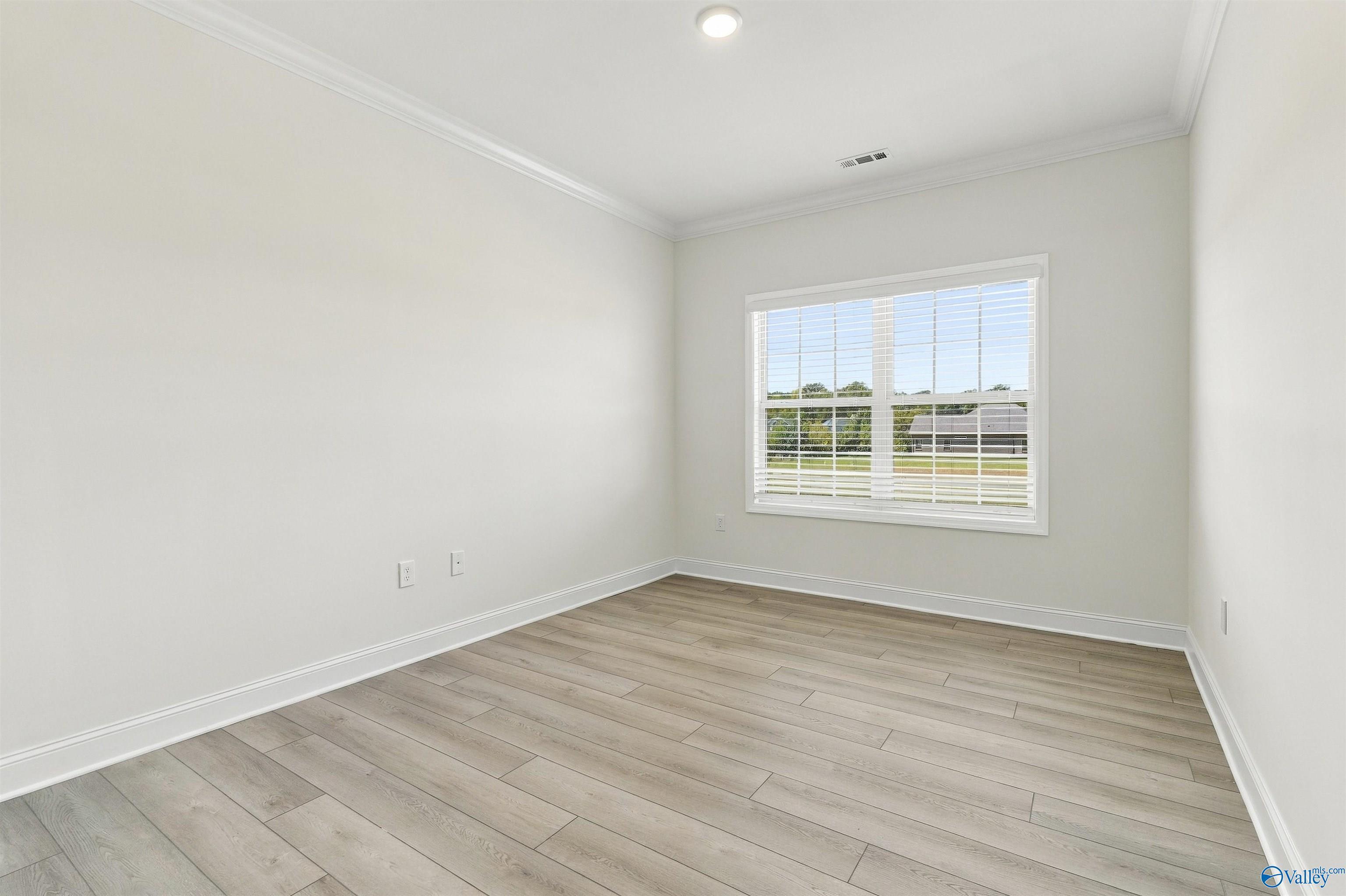 Bright empty bedroom with luxury vinyl plank flooring, white trim, and window with blinds in Davidson Homes The Valencia, Huntsville