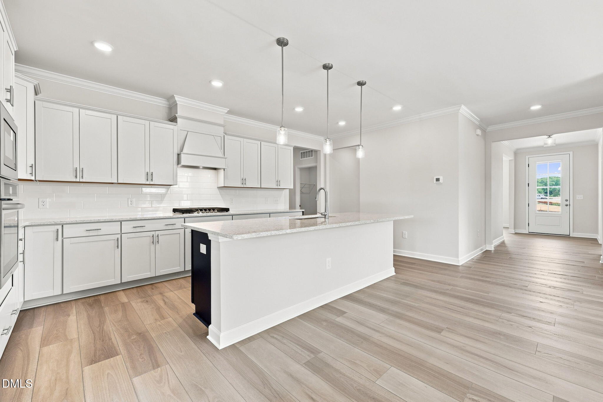 Modern kitchen with white cabinets, granite island, and wood floors in The Magnolia B at Retreat at North Main, Lillington.