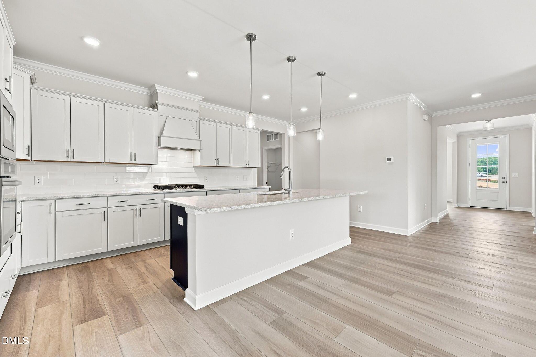 Modern kitchen with white cabinets, granite island, and wood floors in The Magnolia B at Retreat at North Main, Lillington.