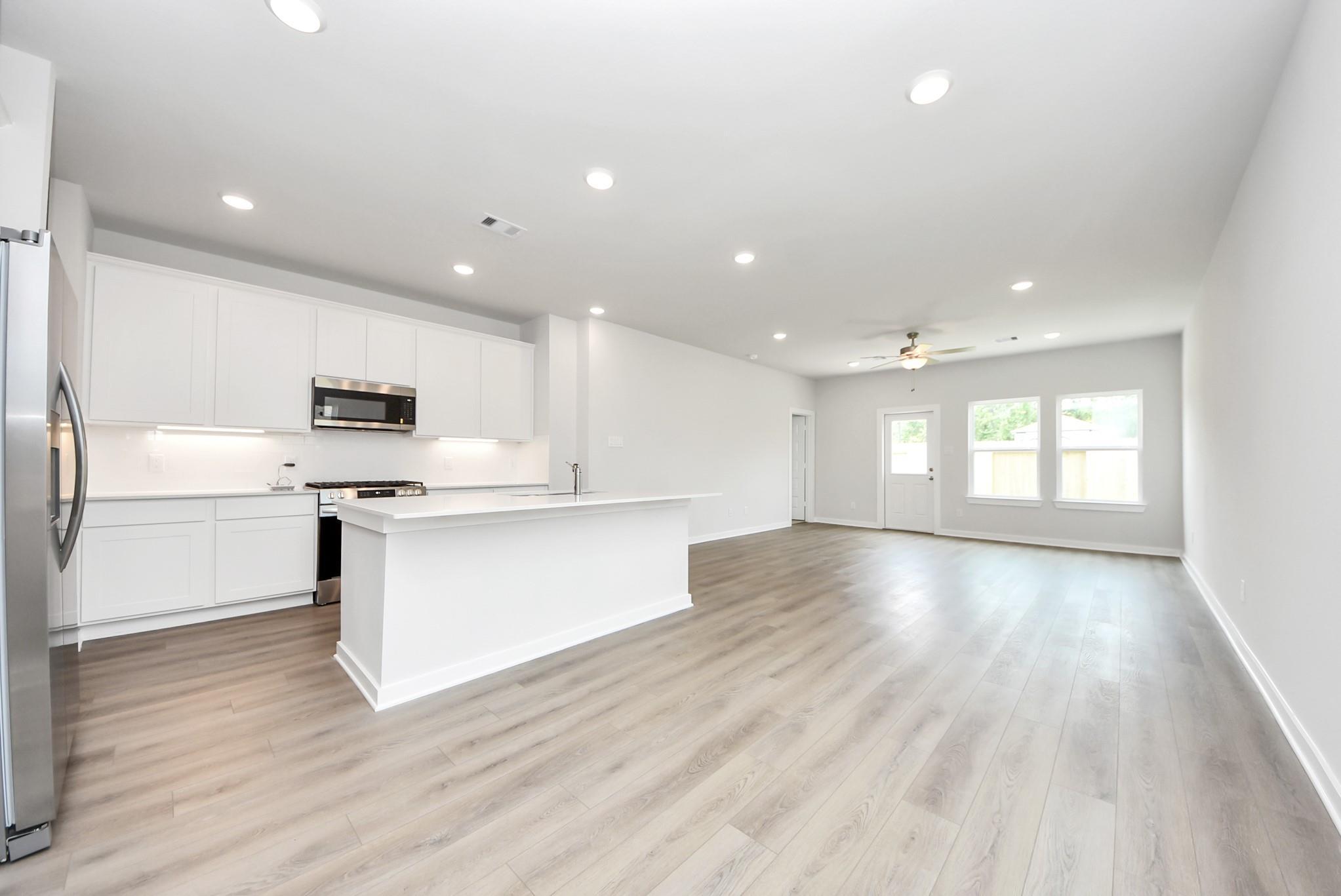 Open-concept kitchen with white cabinets and island in The Blanco E floor plan at The Villages at WestPointe, Dayton, TX.