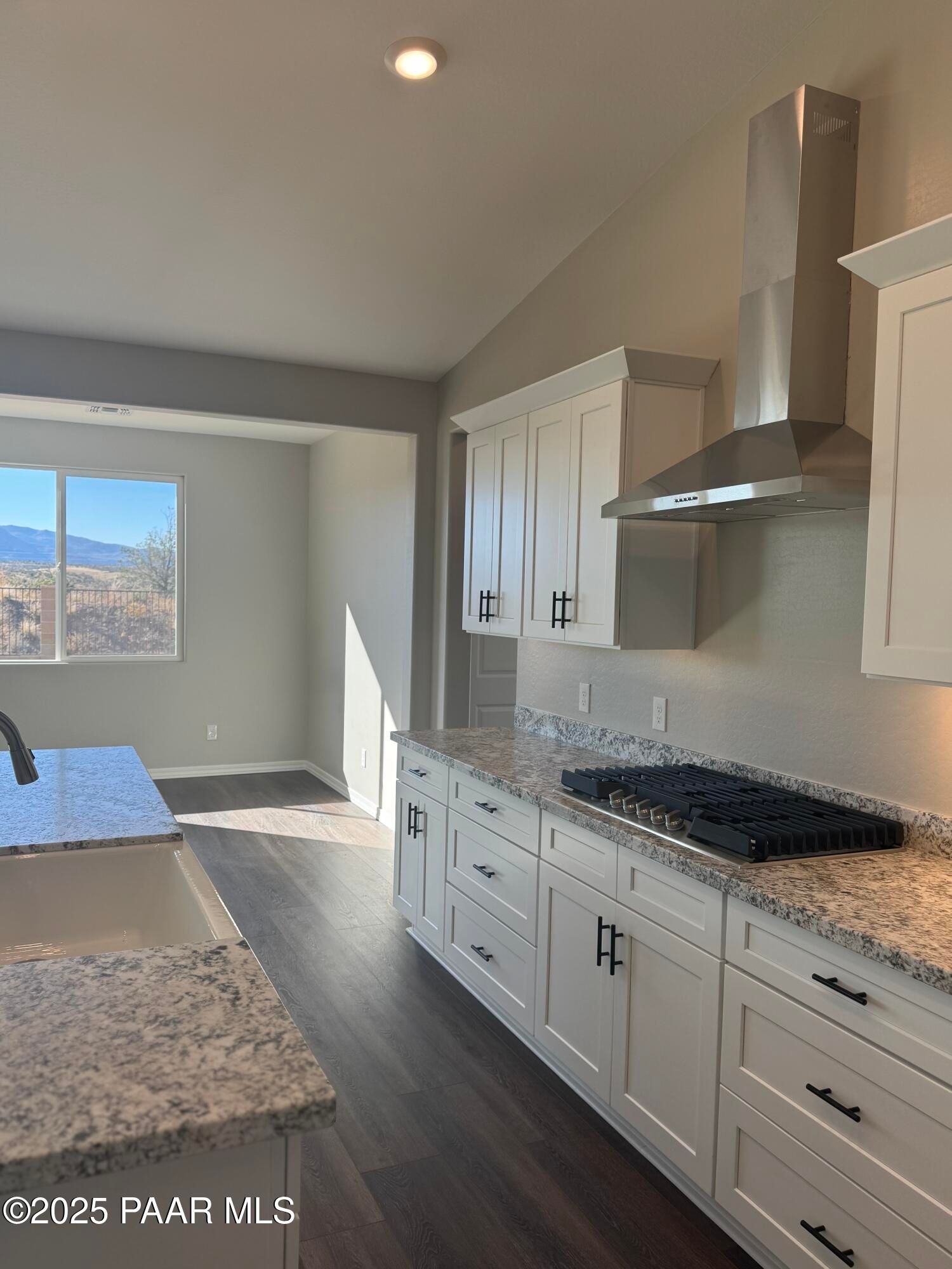 Modern kitchen with white shaker cabinets, granite counters, stainless range hood, and mountain view in Davidson Homes The Monarch E, Prescott Arizona