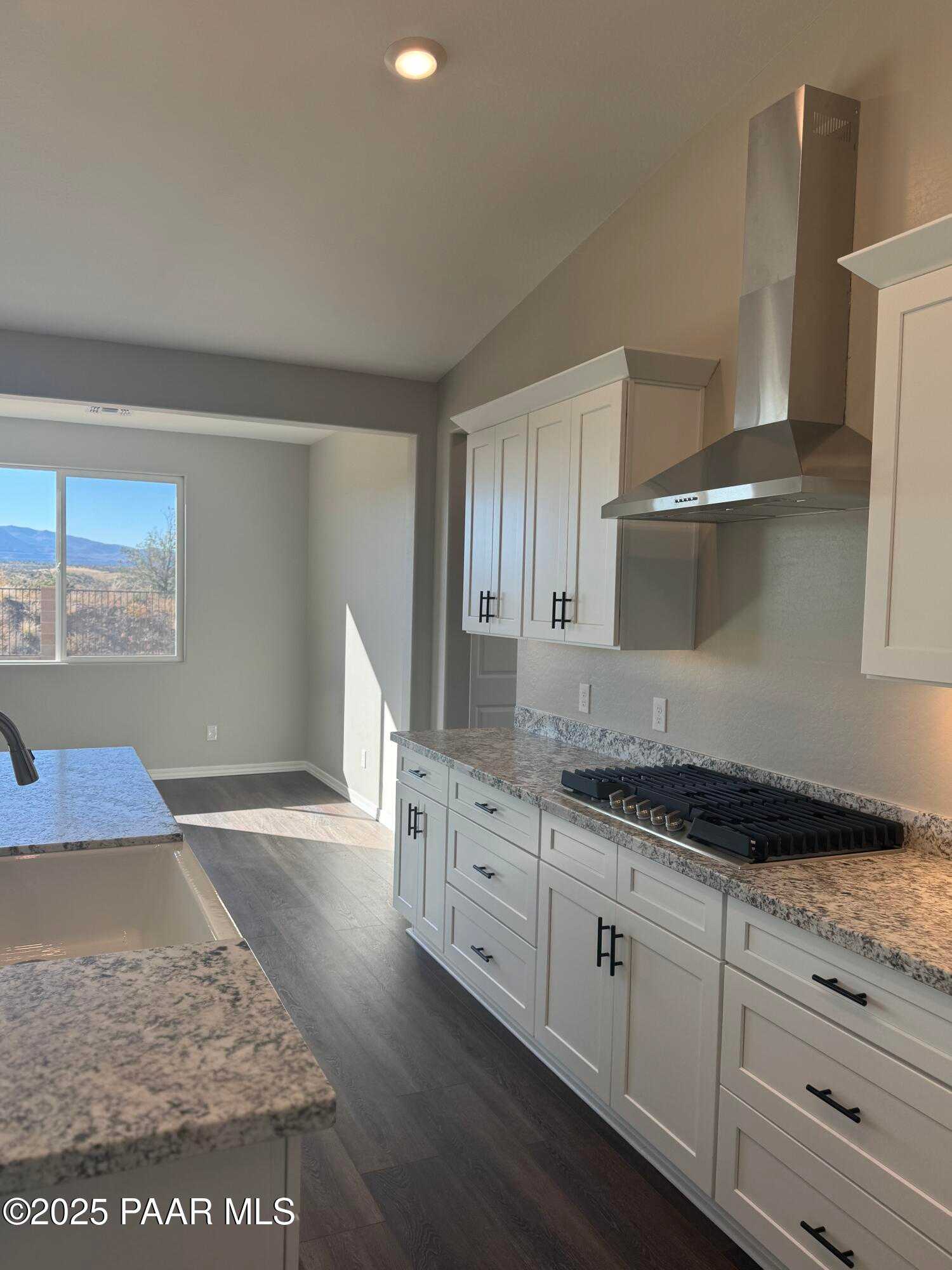 Modern kitchen with white shaker cabinets, granite counters, stainless range hood, and mountain view in Davidson Homes The Monarch E, Prescott Arizona