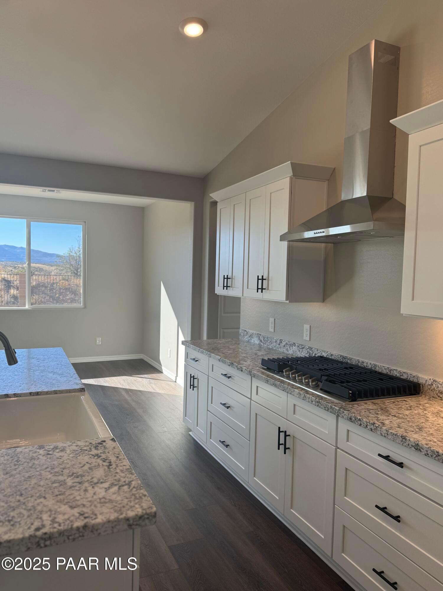 Modern kitchen with white shaker cabinets, granite counters, stainless range hood, and mountain view in Davidson Homes The Monarch E, Prescott Arizona
