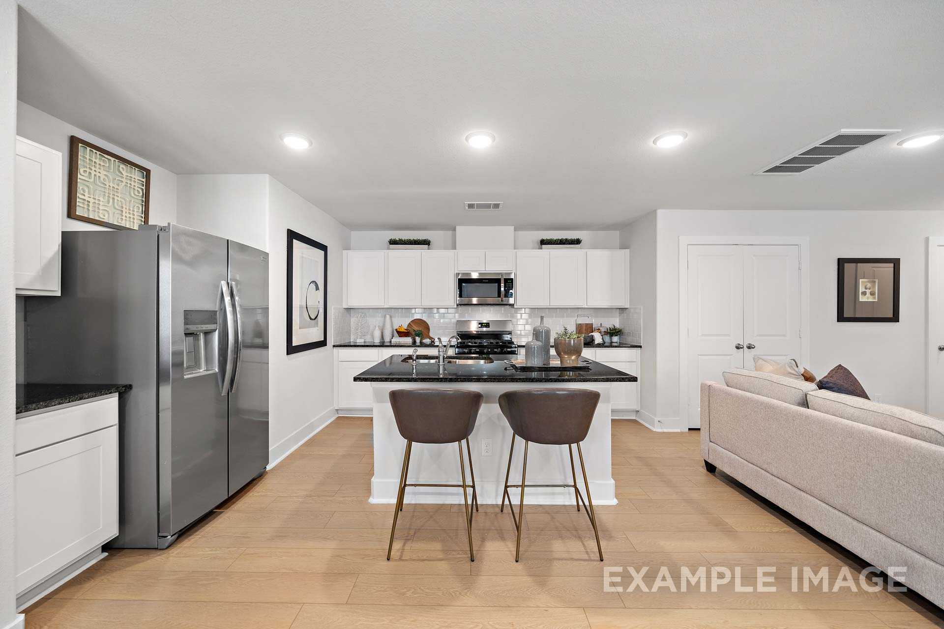 Open-concept kitchen in The Rose B home design with white cabinets, large black island, bar stools, stainless fridge, and living area