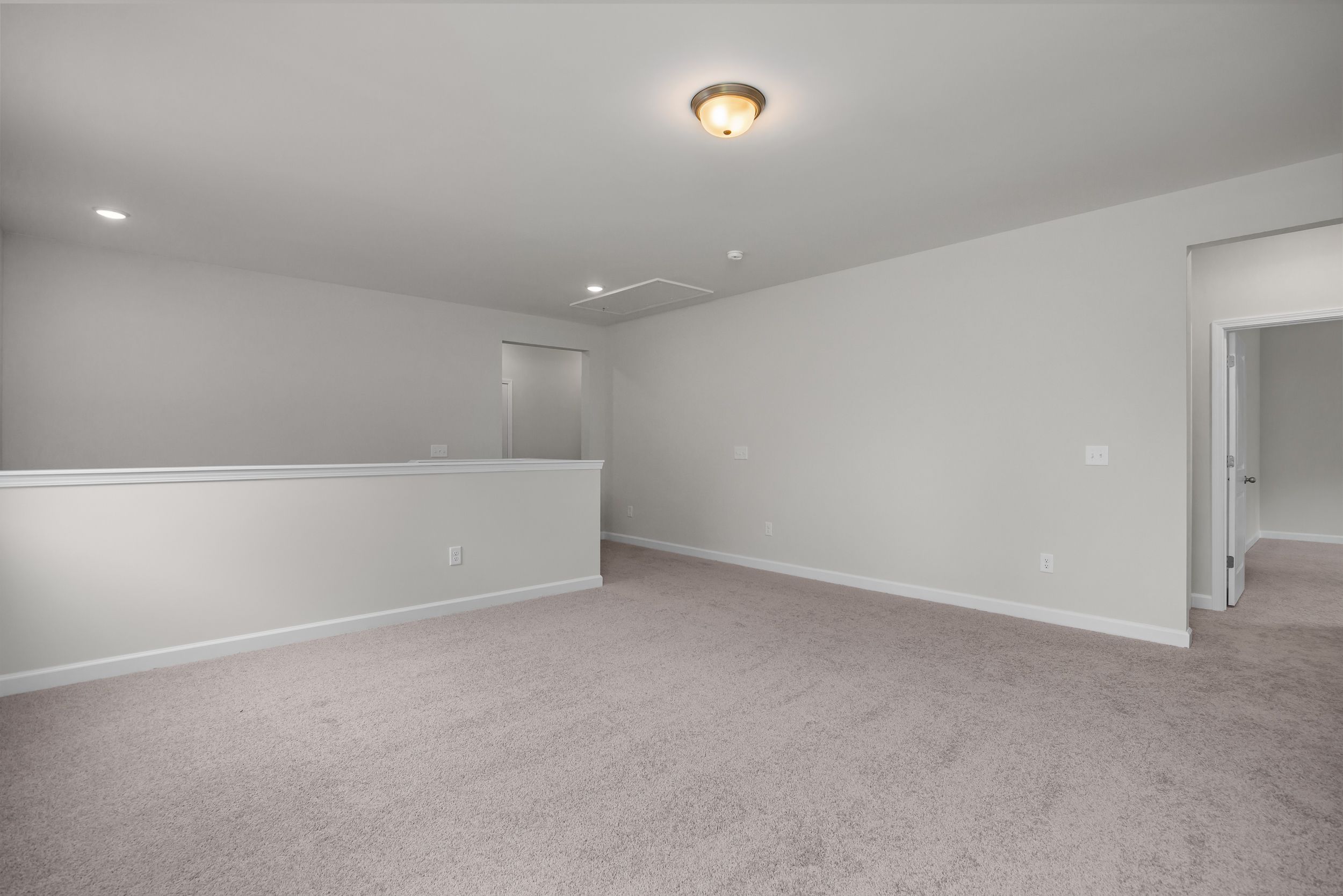 Spacious upper floor hallway in The Aspen Davidson Homes design with light gray walls, beige carpet, and white balcony railing
