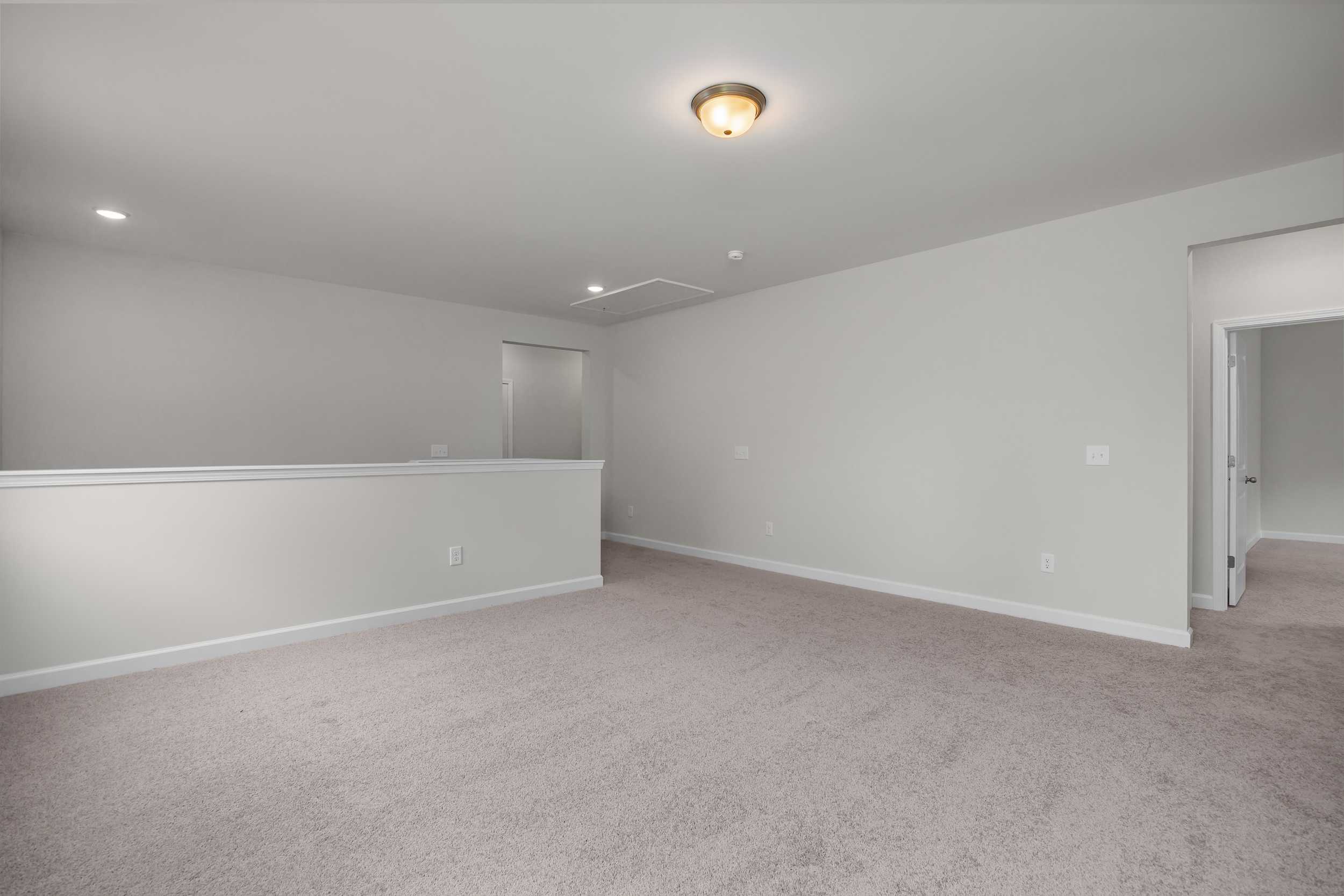 Spacious upper floor hallway in The Aspen Davidson Homes design with light gray walls, beige carpet, and white balcony railing