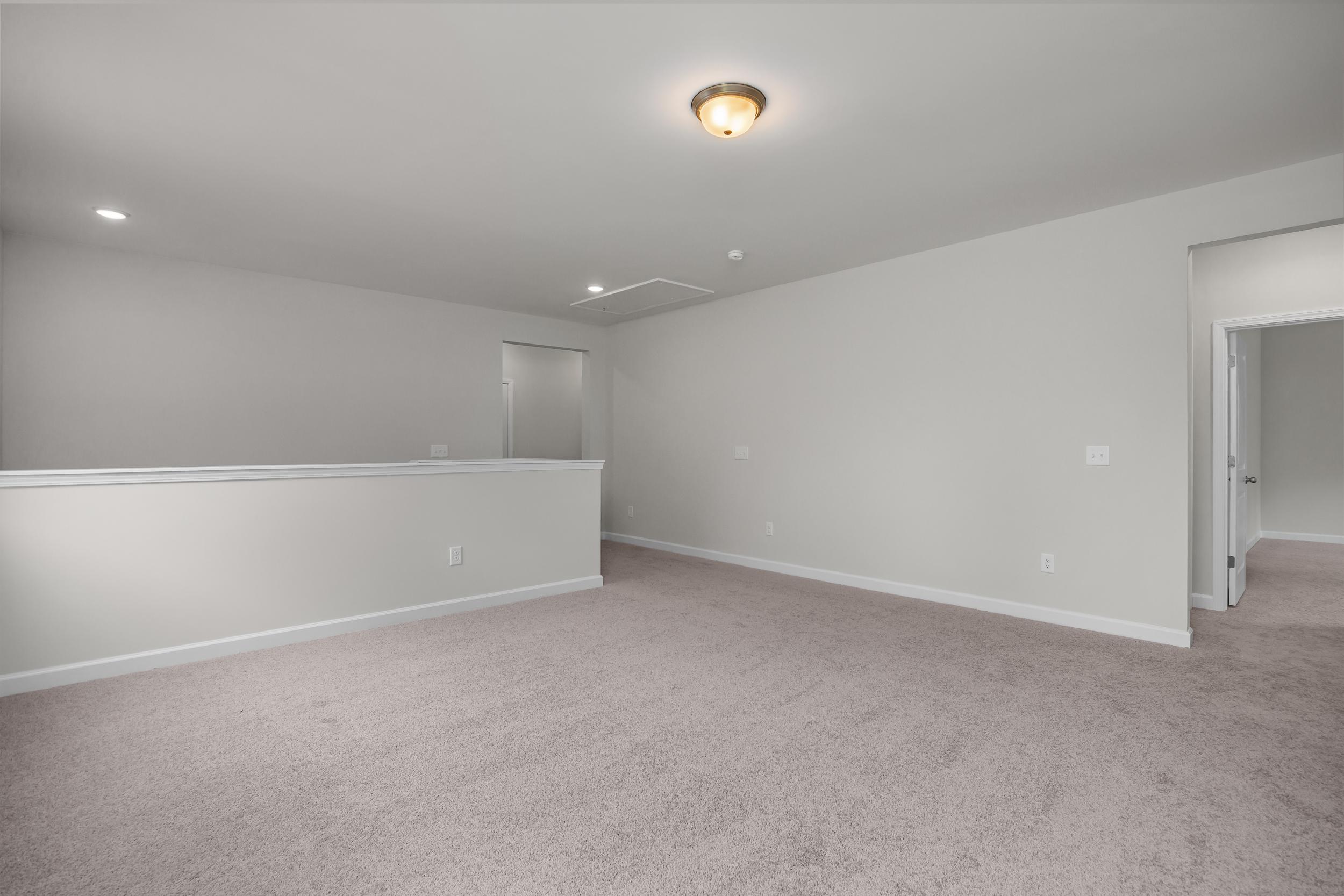 Spacious upper floor hallway in The Aspen Davidson Homes design with light gray walls, beige carpet, and white balcony railing