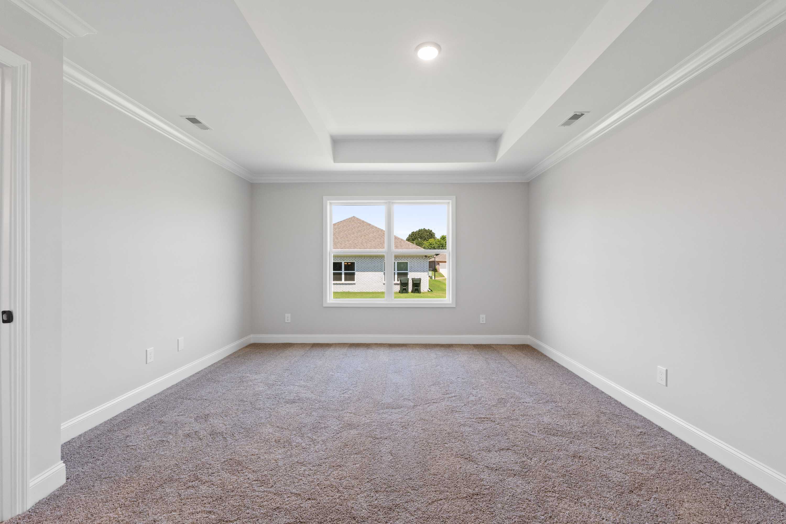 Spacious master bedroom in The Everett C with light gray walls, tray ceiling, large window overlooking backyard, neutral carpet