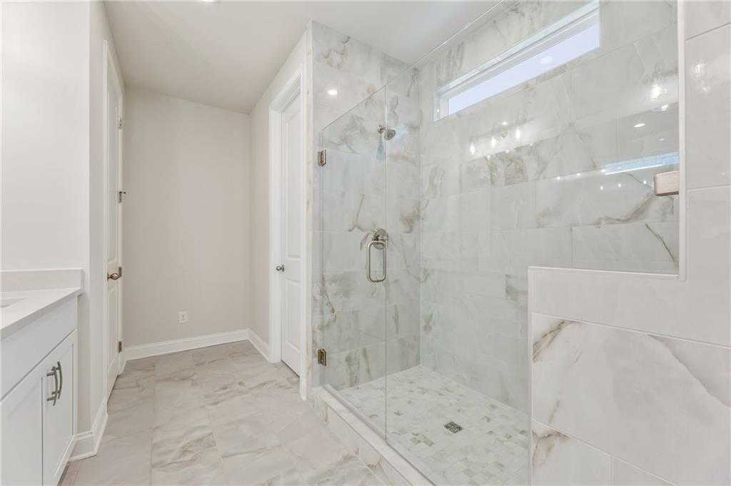 Elegant master bathroom with frameless glass shower, marble tiles, and modern vanity in Davidson Homes The Danbury E, Buford, GA