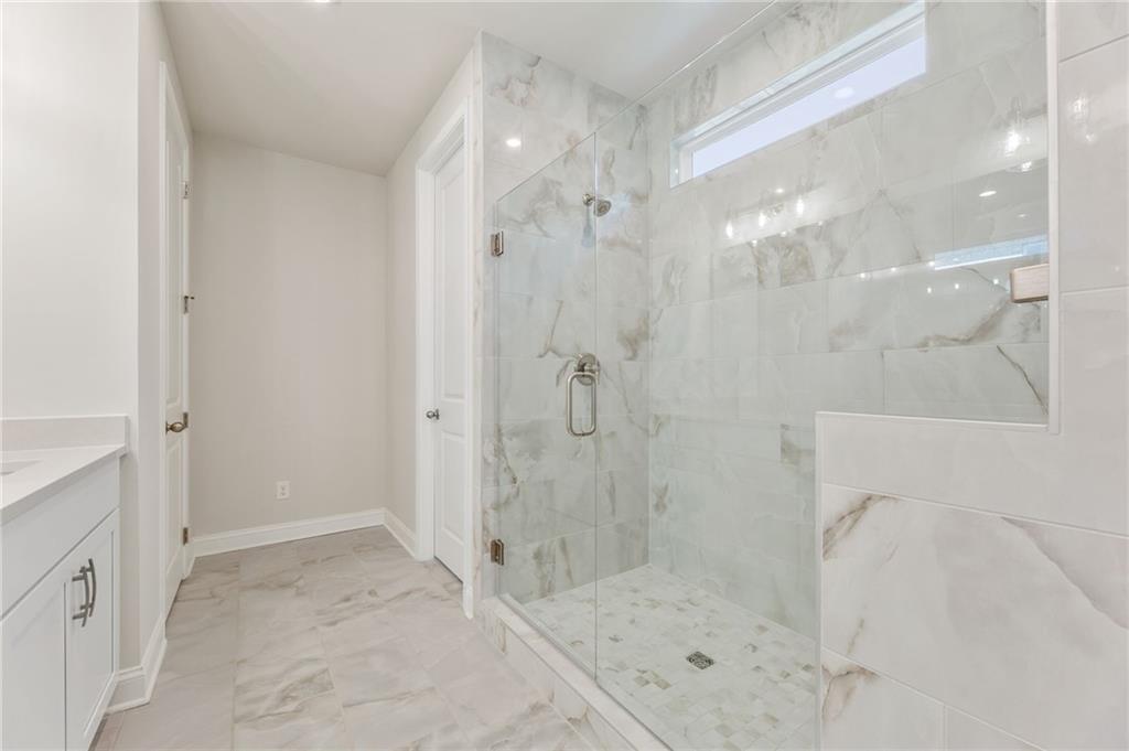 Luxurious master bathroom with white marble shower, frameless glass door, and modern vanity in The Danbury E, Buford, GA