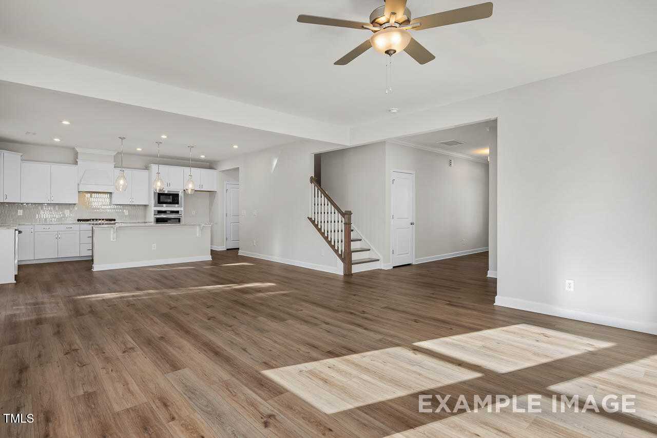 Open-concept kitchen with white cabinets, island, wood floors, and staircase in The Hickory II B by Davidson Homes, Lillington, NC