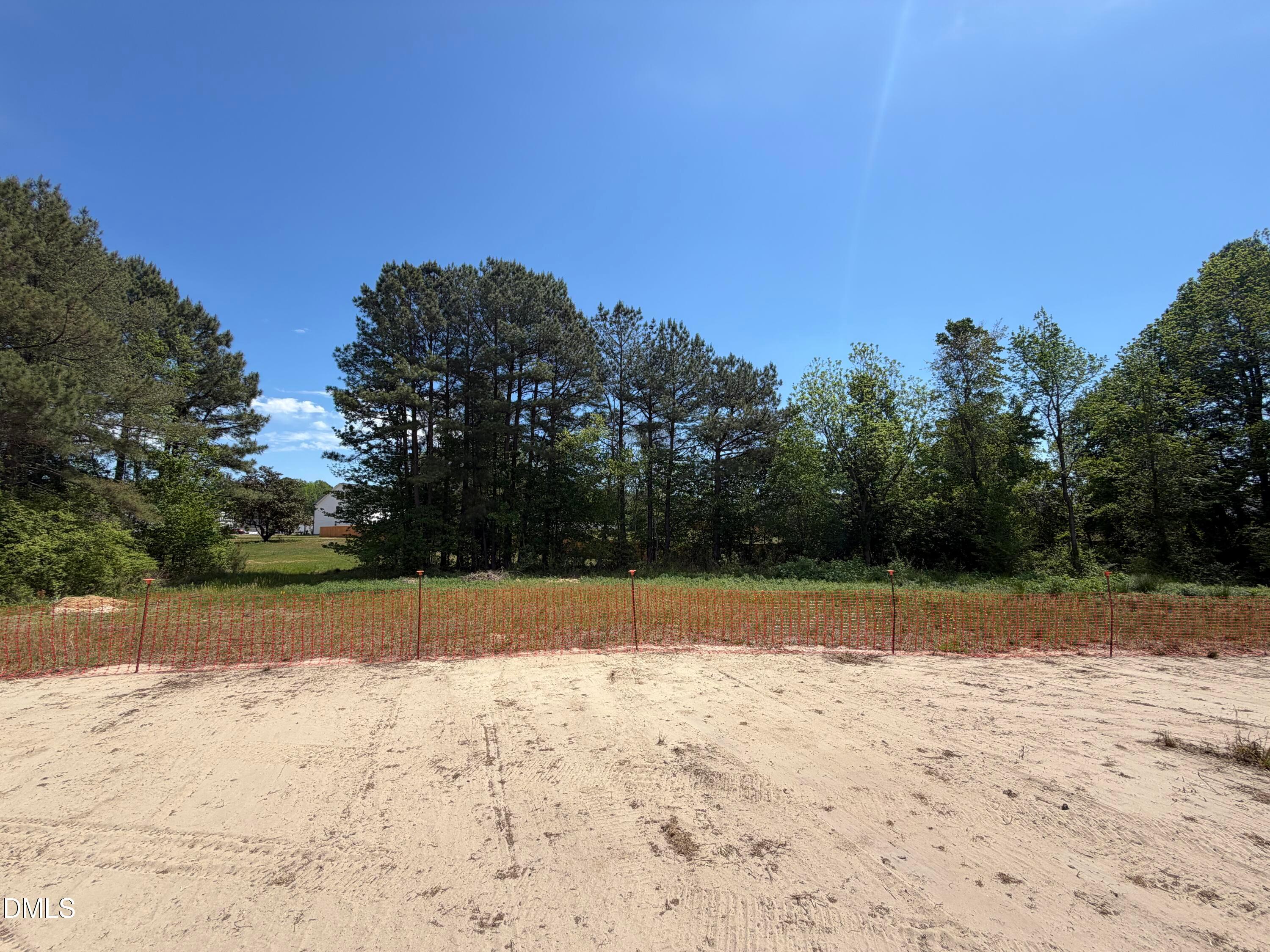 Cleared sandy lot with orange construction fencing amid pine trees under blue sky in Wellers Knoll, Lillington, NC for Davidson Homes Willow D
