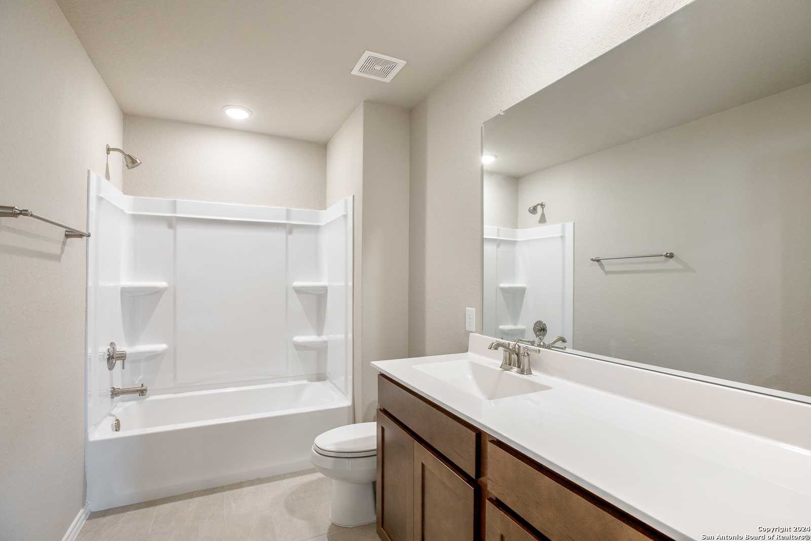 Bright secondary bathroom featuring tub-shower combo, white vanity, and large mirror in Davidson Homes The Murray H, Seguin, Texas