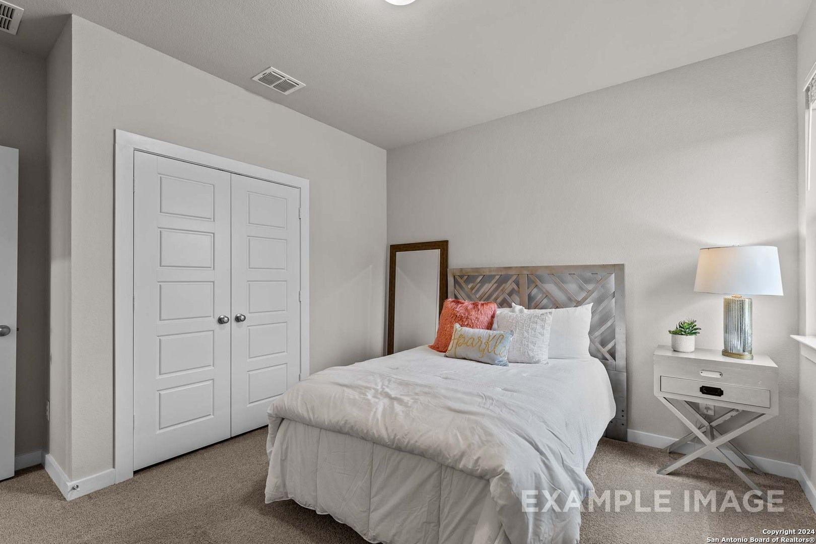 Cozy secondary bedroom with white bed, gray upholstered headboard, orange pillows, bedside lamp in Davidson Homes The Collin A, Seguin, Texas