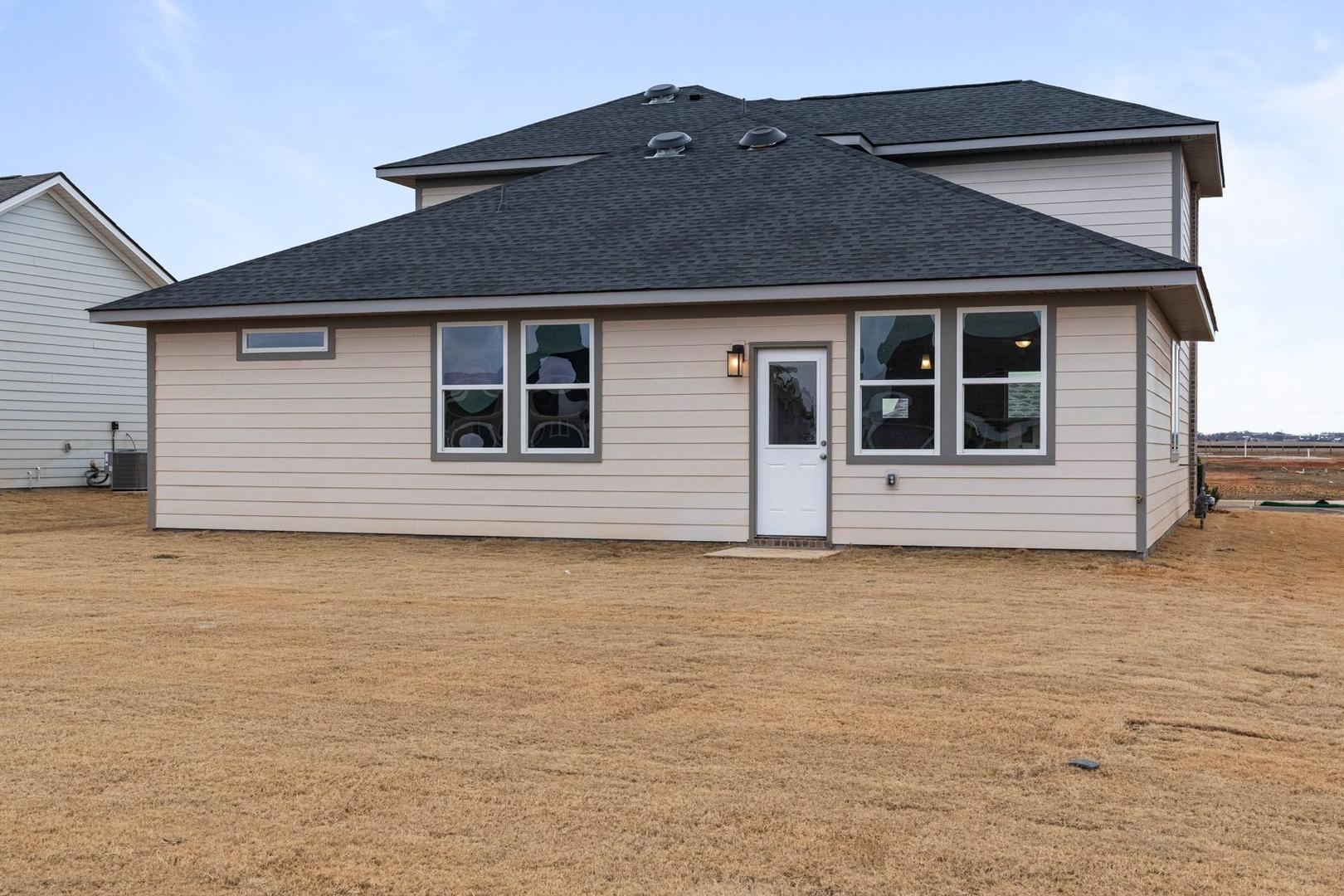 Two-story rear elevation of The Stella A with beige siding, dark shingle roof, large windows, and lantern-lit entry door