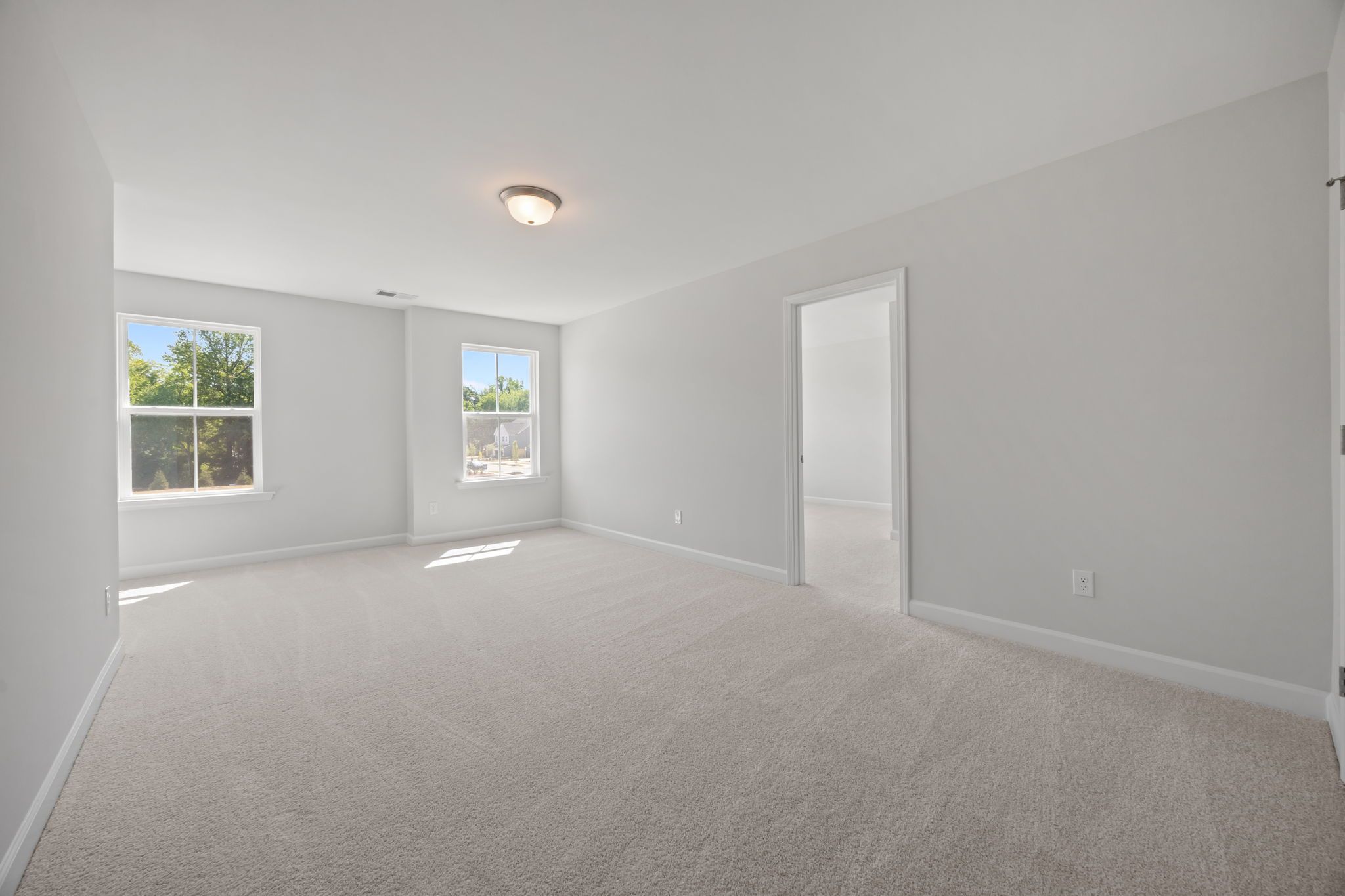 Spacious bedroom in The Ashport B home design featuring neutral carpet, light-filled windows, and an open floor plan.