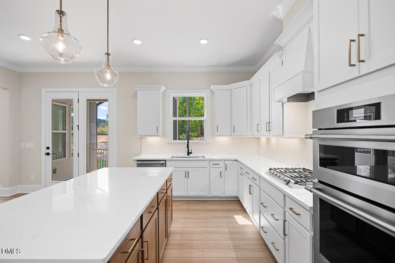 Bright white kitchen with large quartz island, brass pendant lights, and double ovens in Davidson Homes The Crawford D, Wake Forest, NC