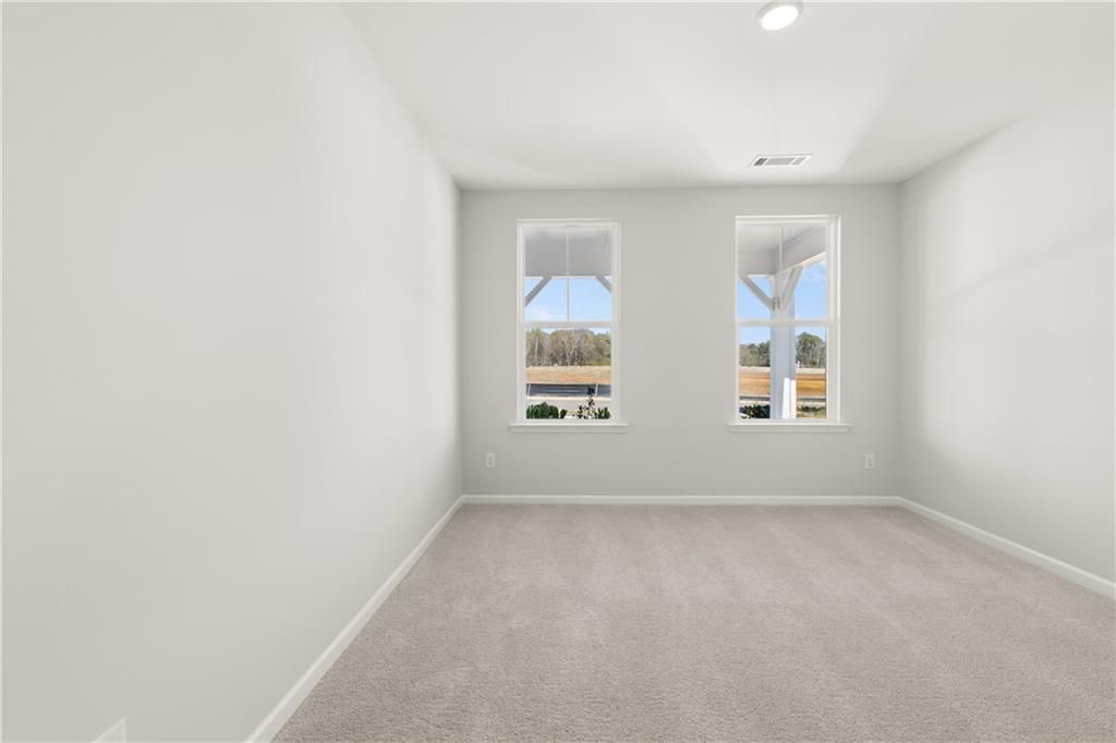 Bright secondary bedroom with gray walls, beige carpet, and dual windows in The Hickory B 5-bedroom home, Winder, Georgia