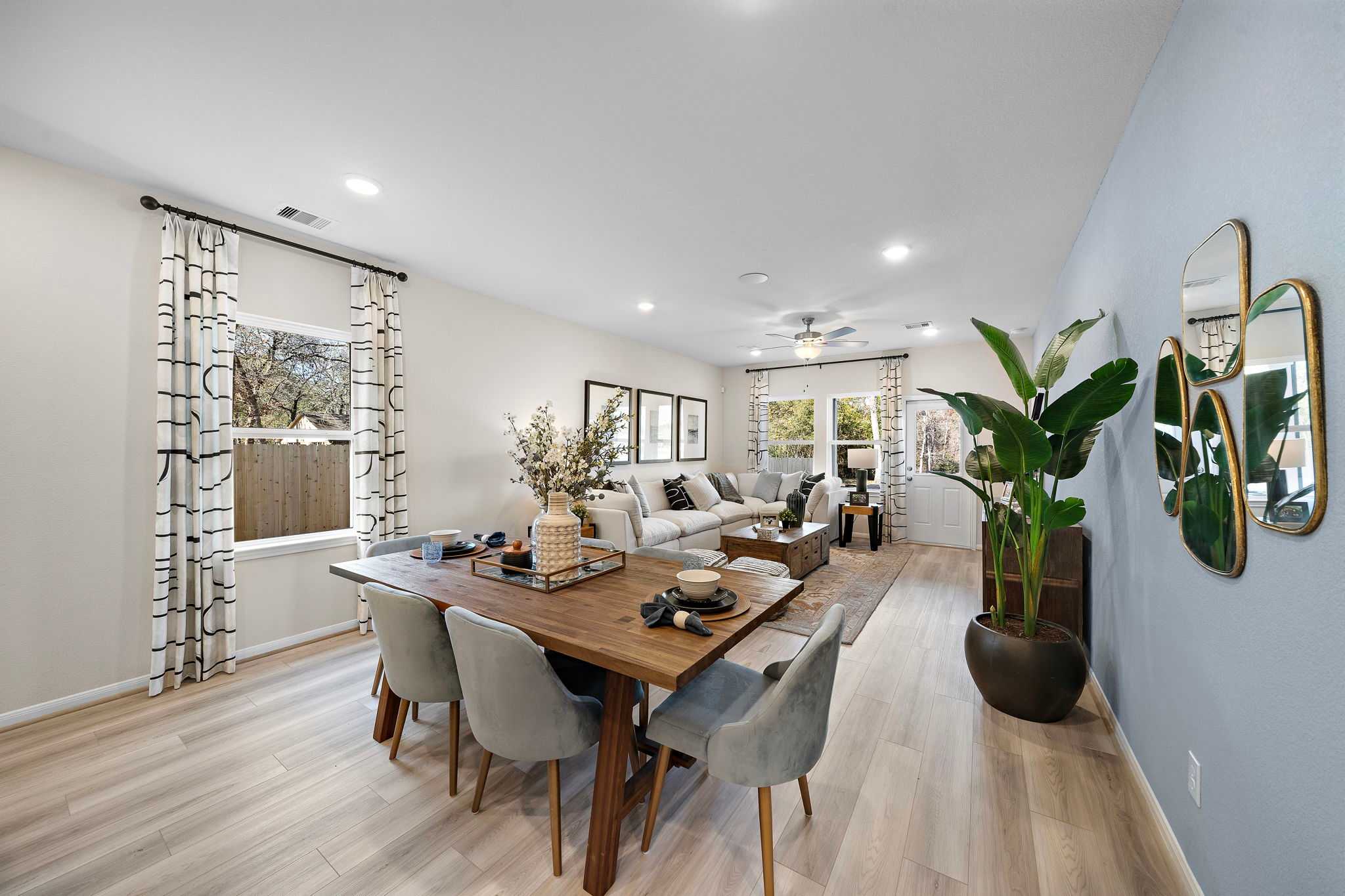 Open-concept living dining room at Lakes at Black Oak in Magnolia TX with hardwood floors, gray sofas, wooden table, and potted plants