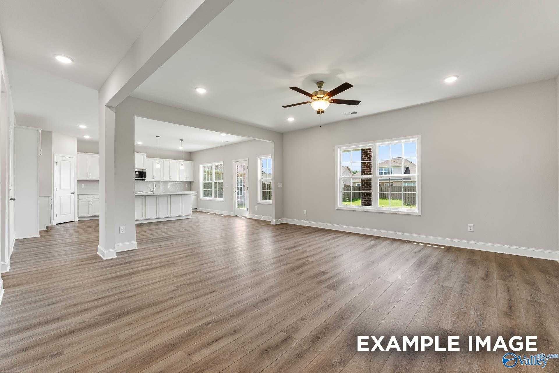 Open-concept kitchen and living room with white cabinets, hardwood floors, ceiling fan, and large windows in Davidson Homes The Madison A, Harvest, Alabama