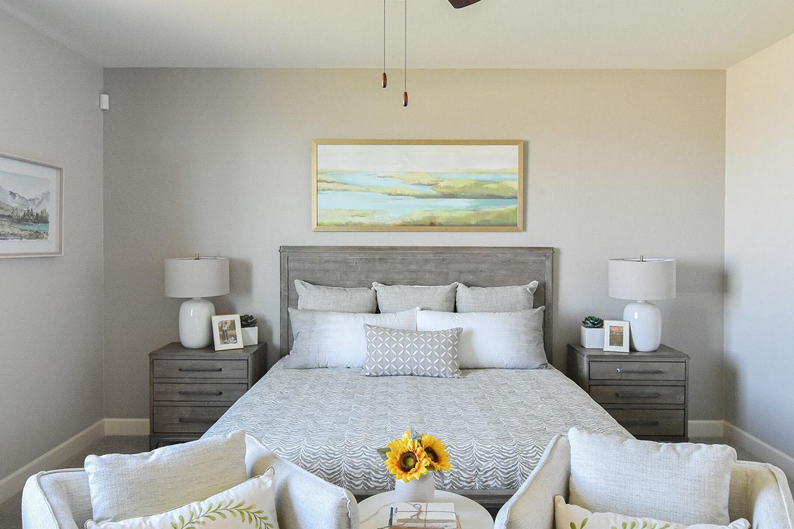 Spacious master bedroom in The Summit E featuring king bed with gray linens, wooden headboard, nightstands, wall art, and armchairs