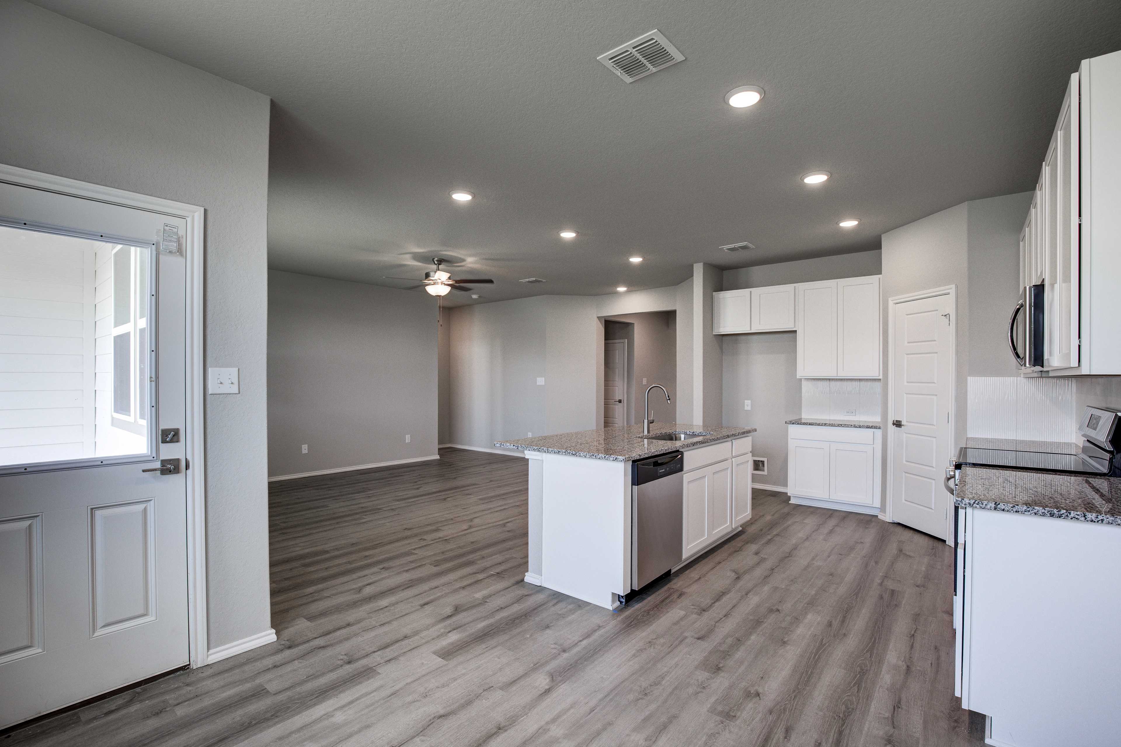 Open-concept kitchen and living area in The Asheville by Davidson Homes, featuring white cabinets, granite island, and luxury vinyl plank flooring