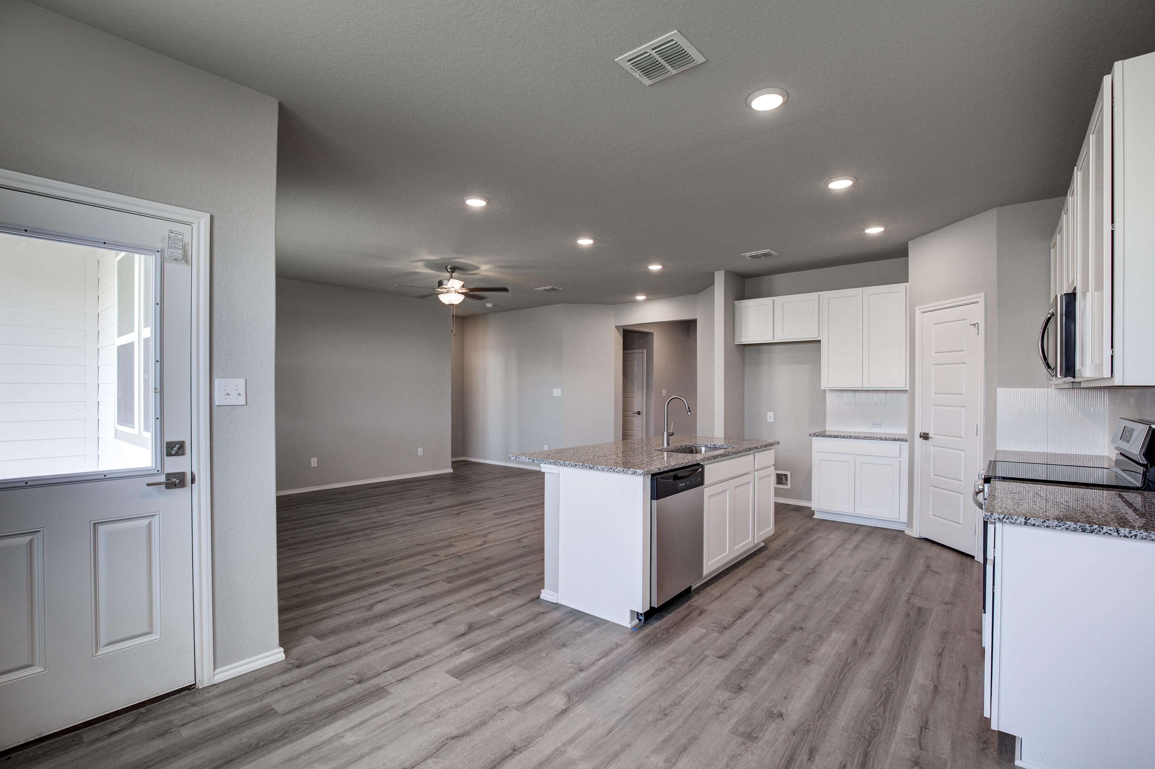 Spacious open-concept kitchen in The Asheville home with white cabinetry, granite island sink, dishwasher, and adjacent living area featuring ceiling fan and luxury vinyl plank flooring
