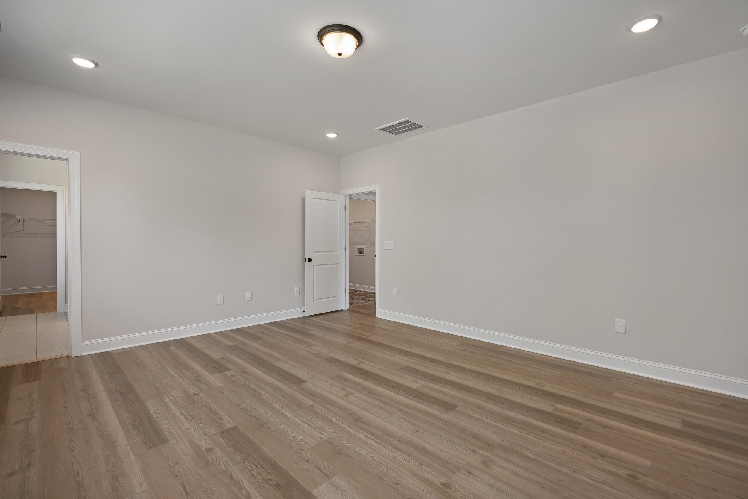 Spacious empty bedroom with light gray walls, luxury vinyl plank floors, and en-suite bathroom at Rockport in Wake Forest NC by Davidson Homes