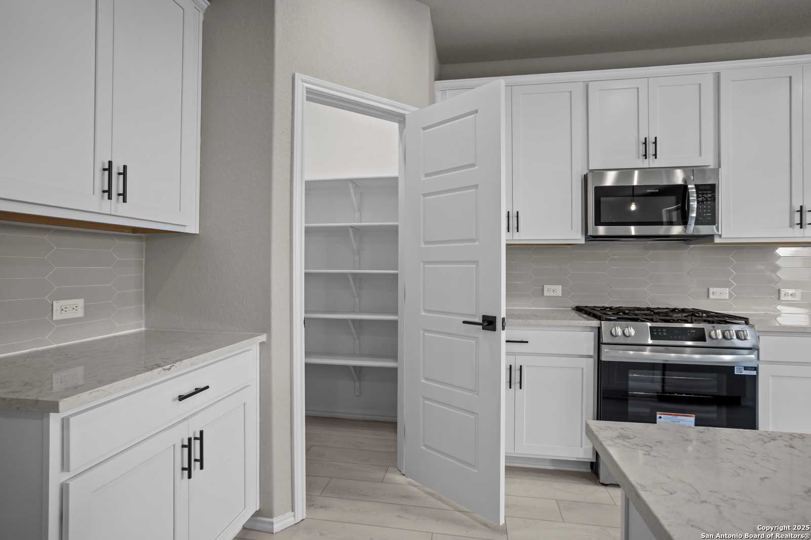 Modern kitchen featuring white shaker cabinets, granite counters, stainless appliances, and open walk-in pantry in The Asheville E, Converse, Texas