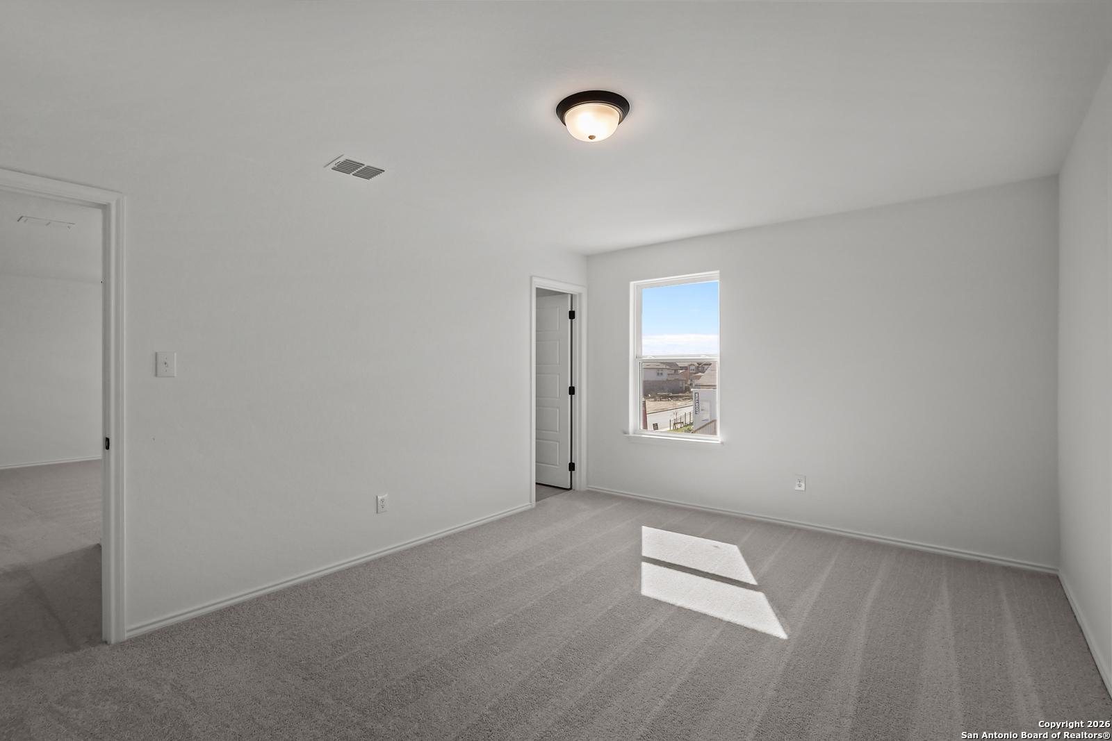 Bright secondary bedroom with white walls, gray carpet, and large window in Davidson Homes The Douglas E, San Antonio