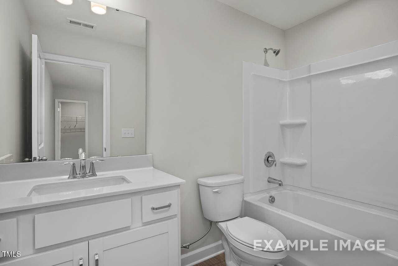 Modern bathroom featuring white vanity, walk-in shower, bathtub, and toilet in Davidson Homes The Hickory II B, Lillington, NC