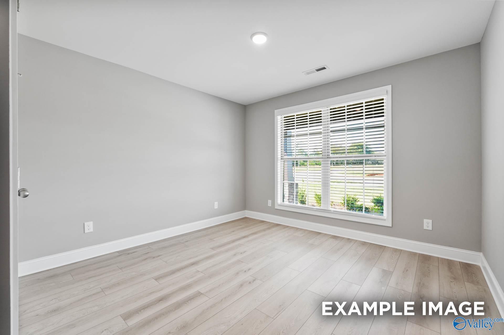 Bright empty bedroom with light gray walls, laminate wood floors, large window and blinds in Davidson Homes The Everett B, Toney, Alabama