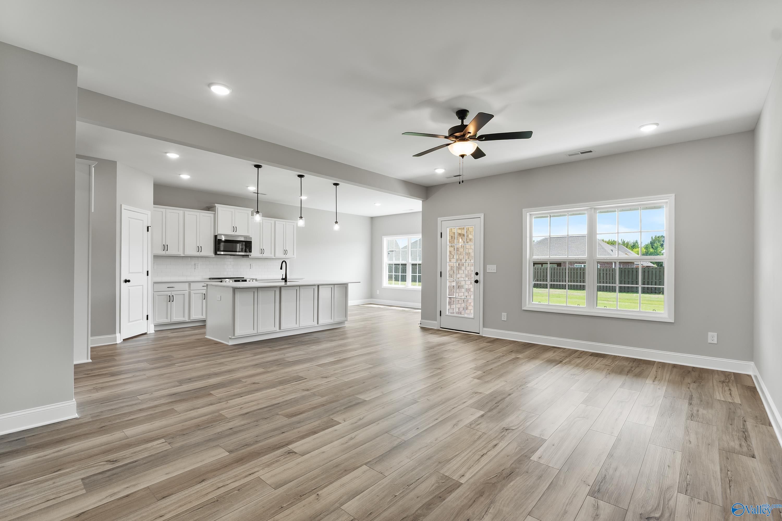 Open-concept living room and kitchen with white island, pendant lights, ceiling fan, and large windows in Davidson Homes The Montgomery B With Bonus, Toney, Alabama