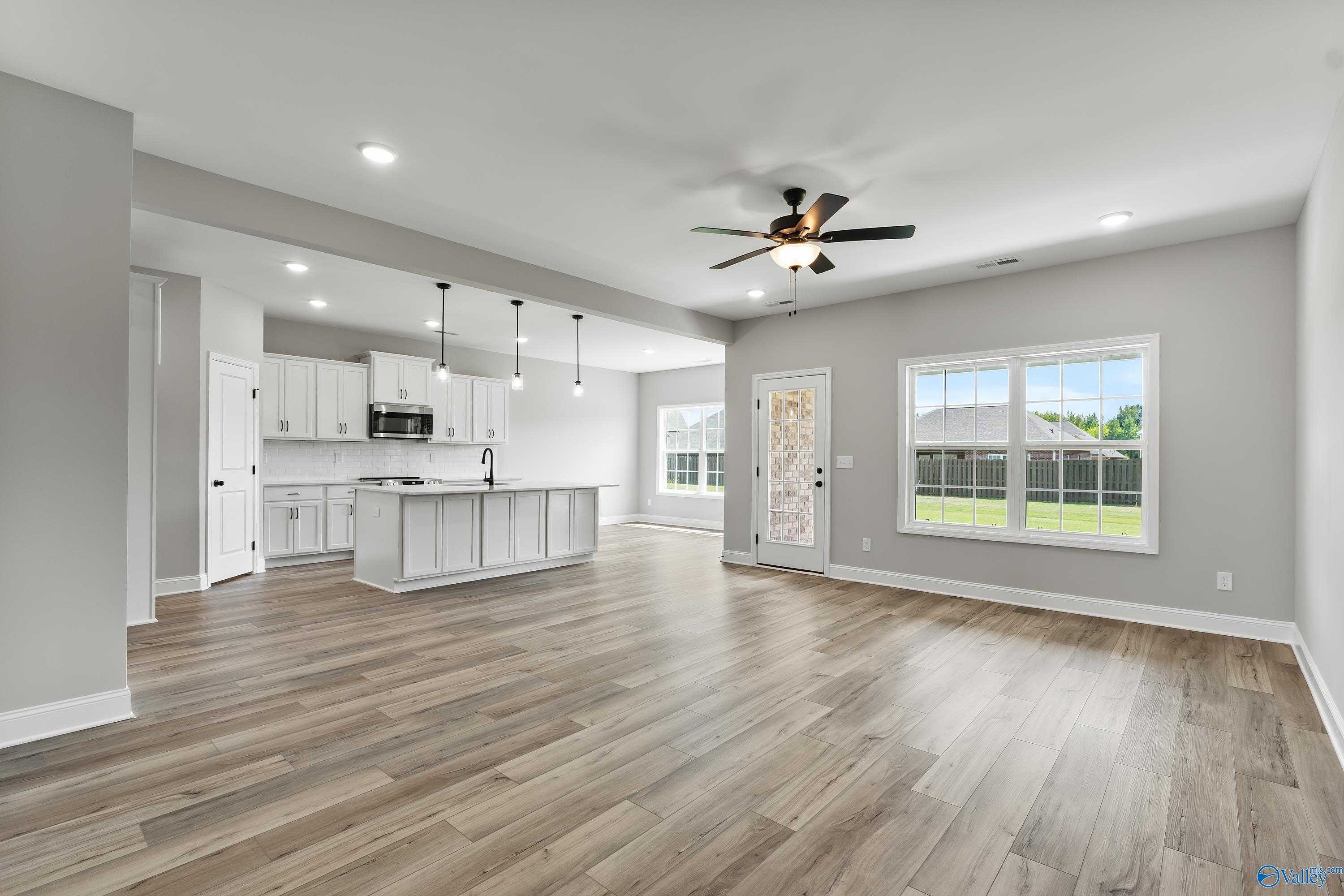 Spacious open kitchen with white island, stainless appliances, hardwood floors, and living area ceiling fan overlooking backyard in Davidson Homes Montgomery B With Bonus, Toney, Alabama