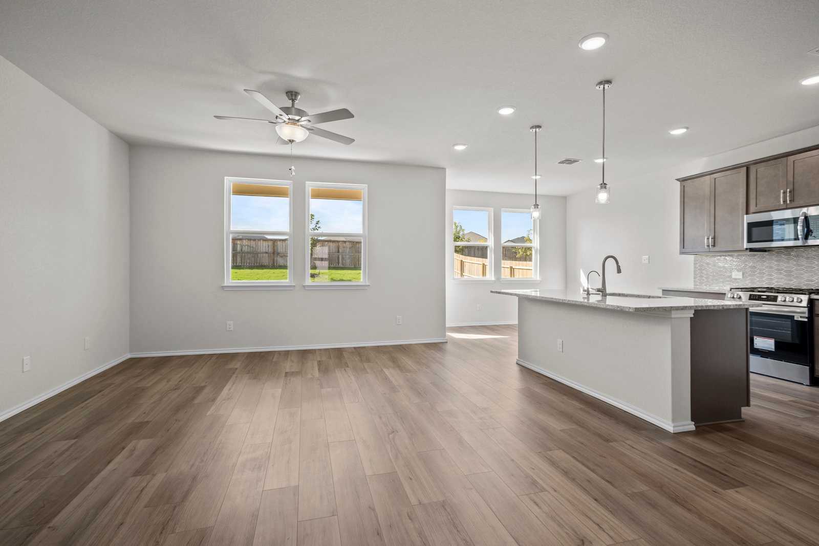 Open-concept living kitchen with wood floors, ceiling fan, stainless appliances, and backyard view in Davidson Homes Redbud B, Josephine, TX