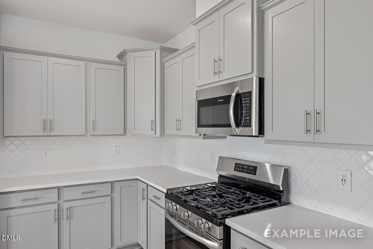 Modern kitchen featuring white cabinets, stainless steel microwave, oven, and gas cooktop with subway tile backsplash in The Daphne C by Davidson Homes, Zebulon, NC