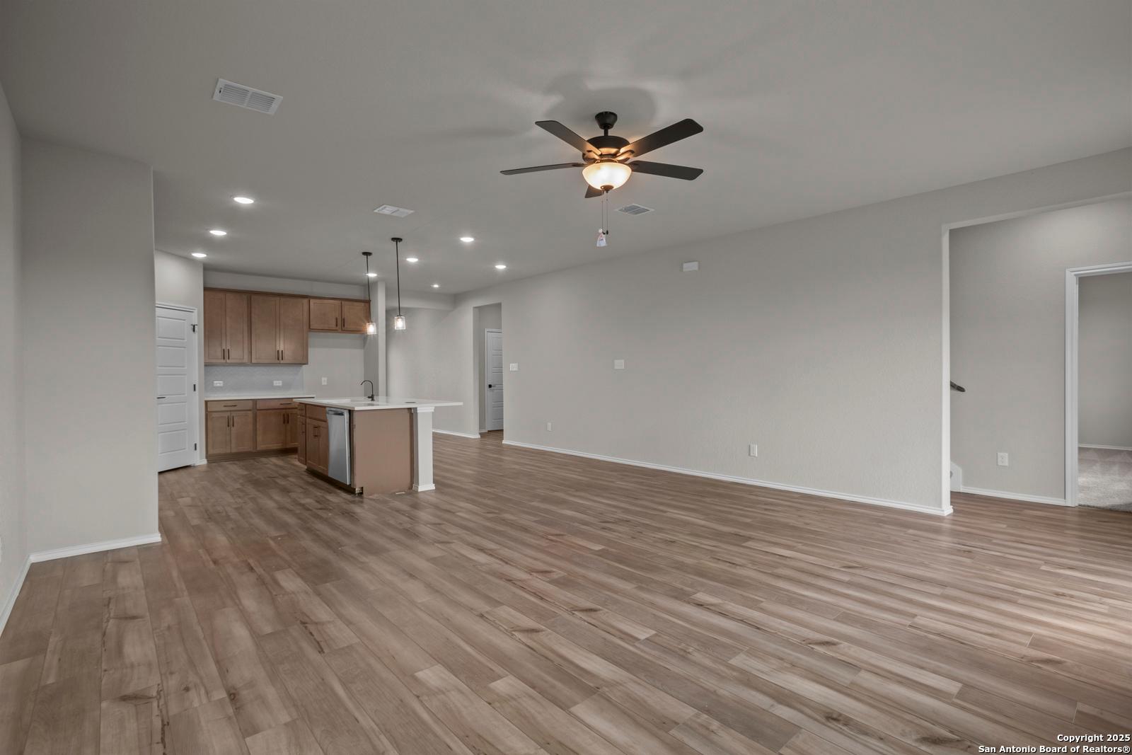Open-concept kitchen and living area with wooden cabinets, island, hardwood floors, and ceiling fans in Davidson Homes The Douglas F, San Antonio