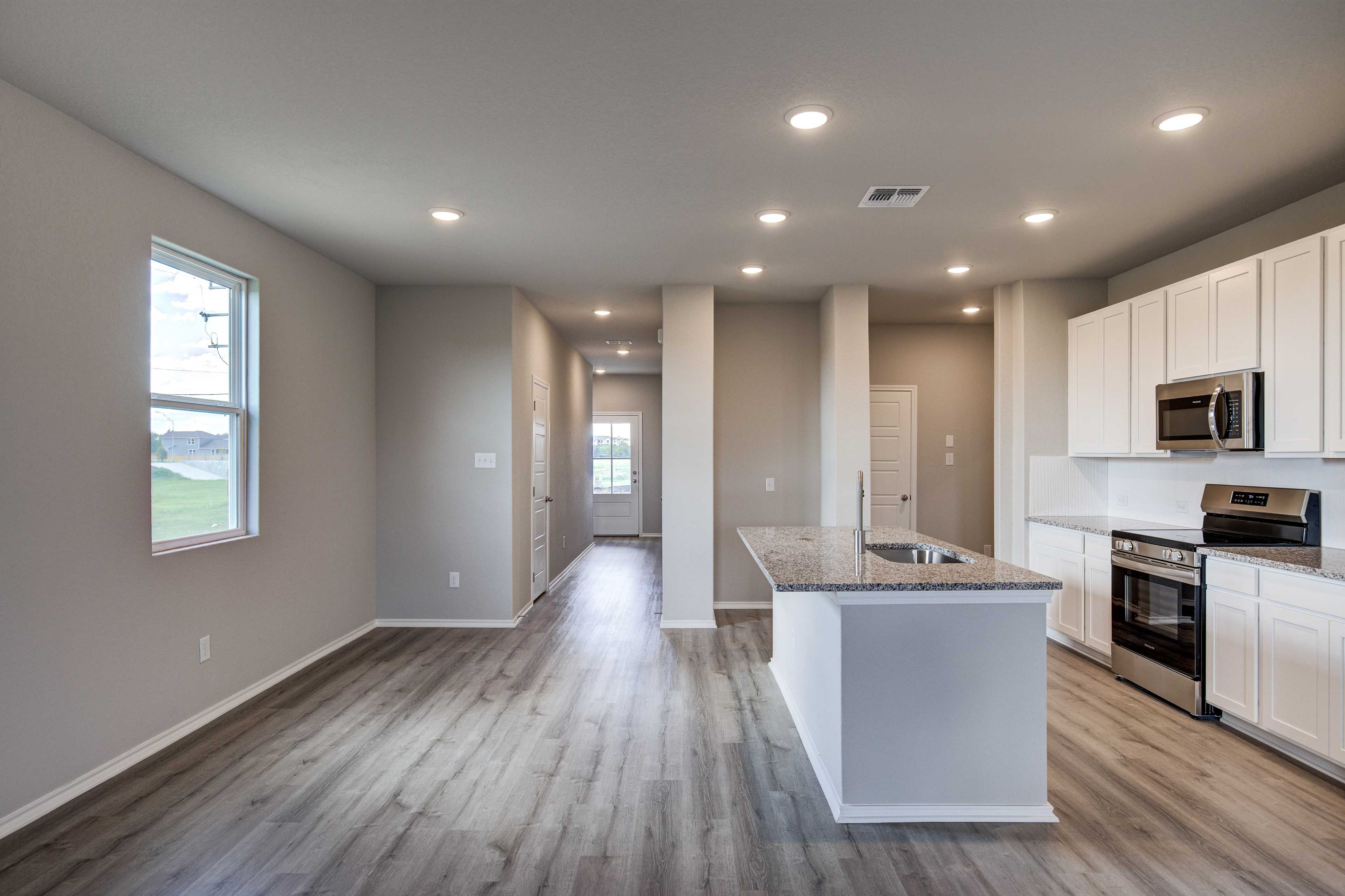Spacious open-concept kitchen in The Blanco B featuring white cabinets, granite island, stainless appliances, and hardwood floors