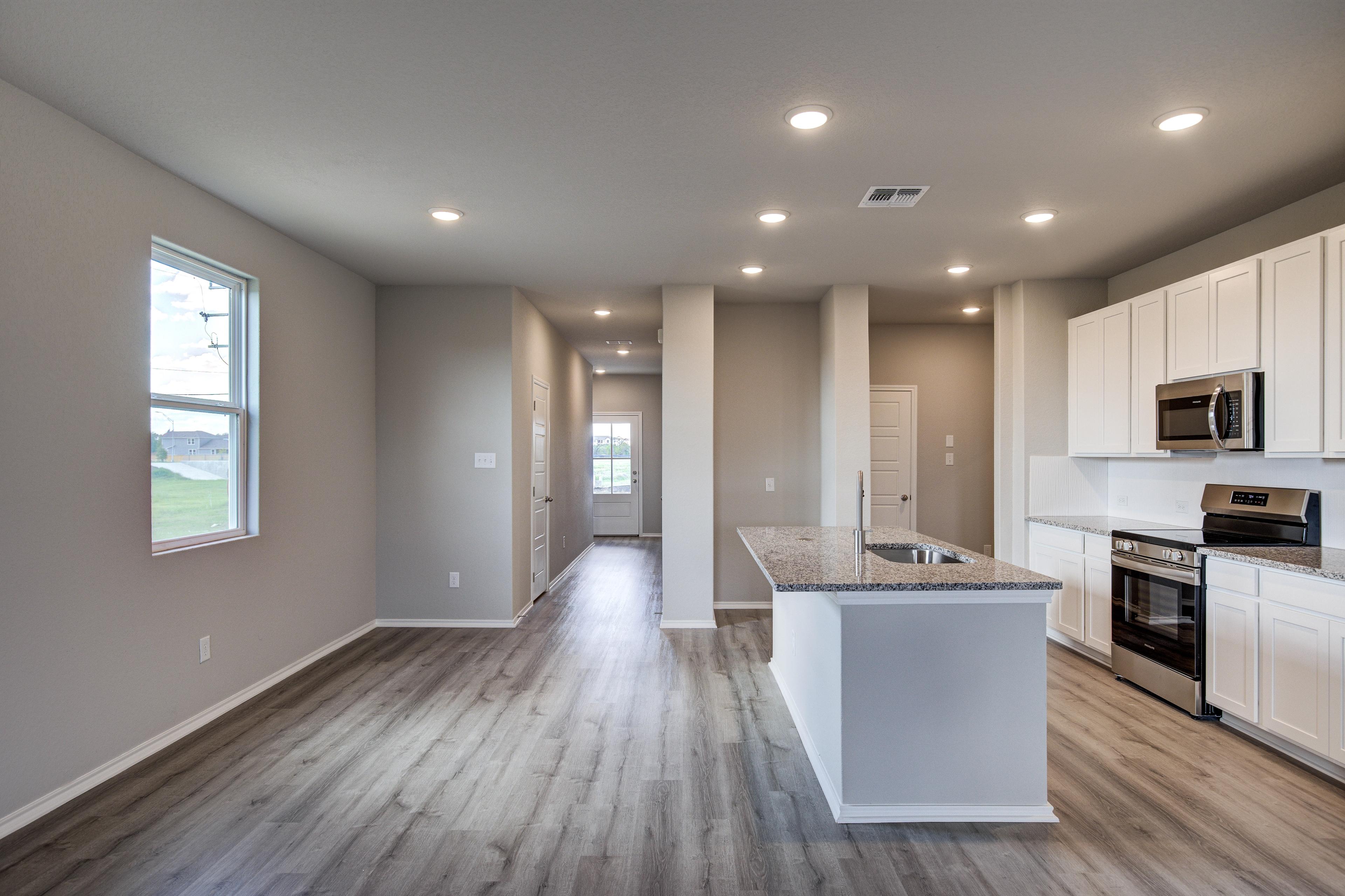 Spacious open-concept kitchen in The Blanco C showcasing white cabinets, granite island, stainless appliances, and hardwood floors