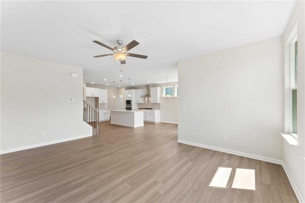 Open-concept living and kitchen with white island, stainless appliances, and ceiling fan in Davidson Homes The Ash B plan, Riverwood, GA