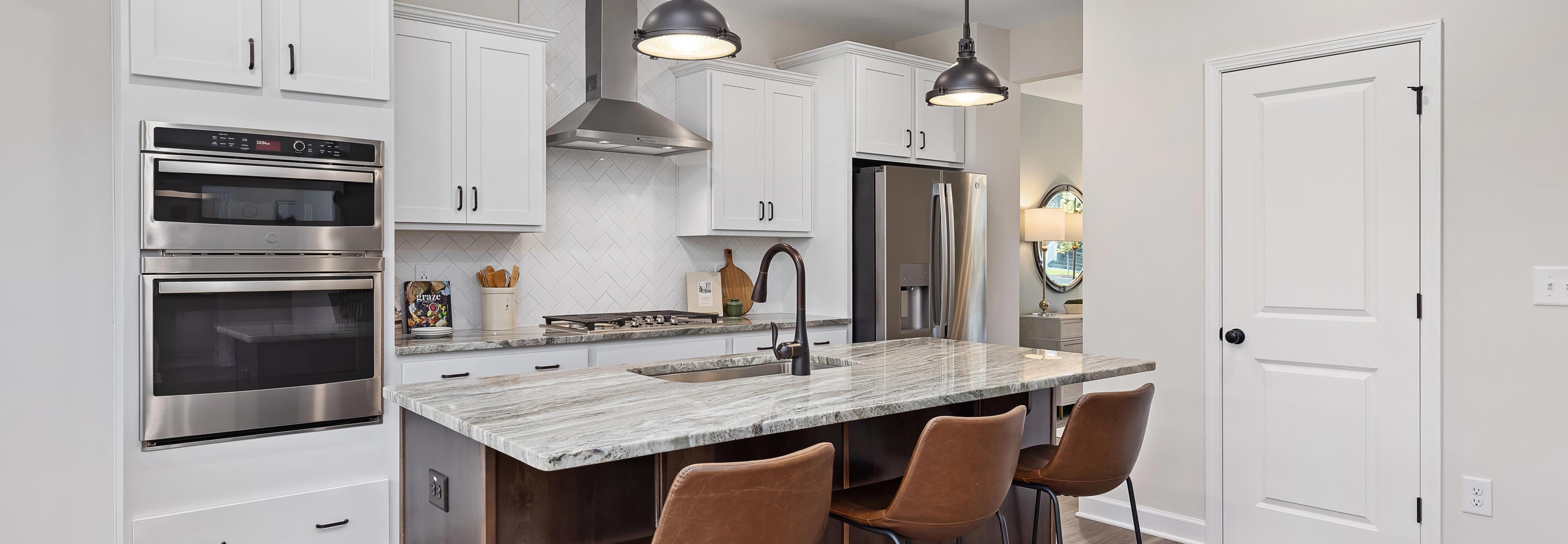 Spacious modern kitchen at Woodland Crossing in Zebulon NC with white shaker cabinets, quartz island, leather bar stools, stainless appliances
